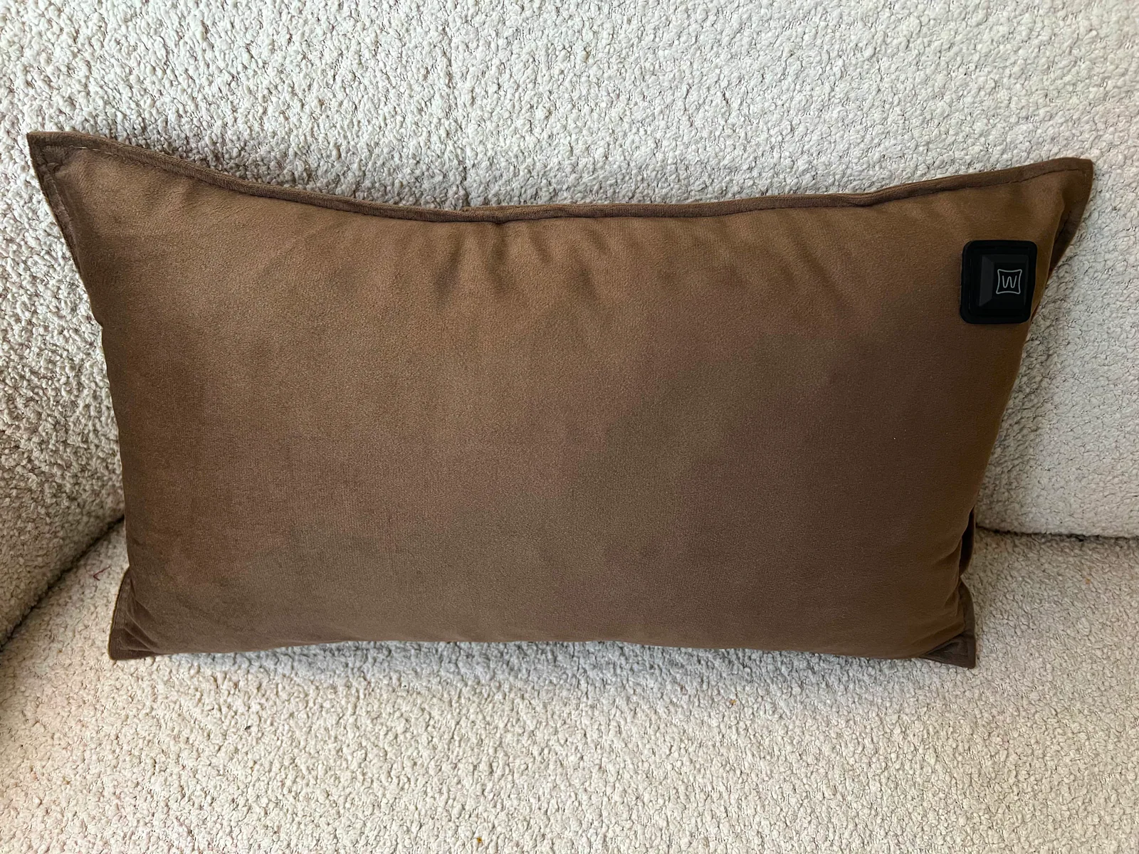 Ein braunes Kissen mit schwarzem Etikett in der Ecke ruht auf einer strukturierten beigen Oberfläche.