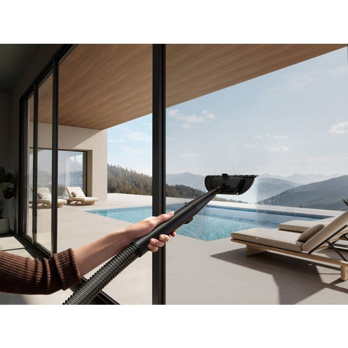 Fensterreiniger sprüht Wasser auf ein großes Fenster mit Blick auf einen Pool und Berge.