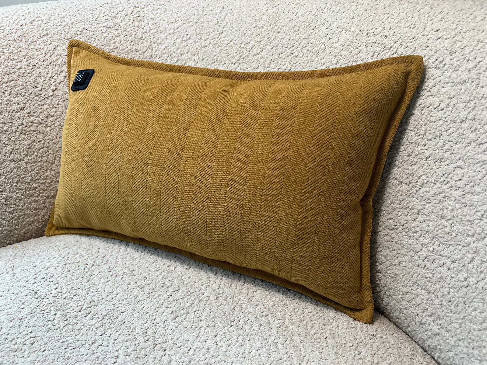 Ein ockergelbes Kissen mit Fischgrätenmuster liegt auf einem hellgrauen Bouclé-Sofa.