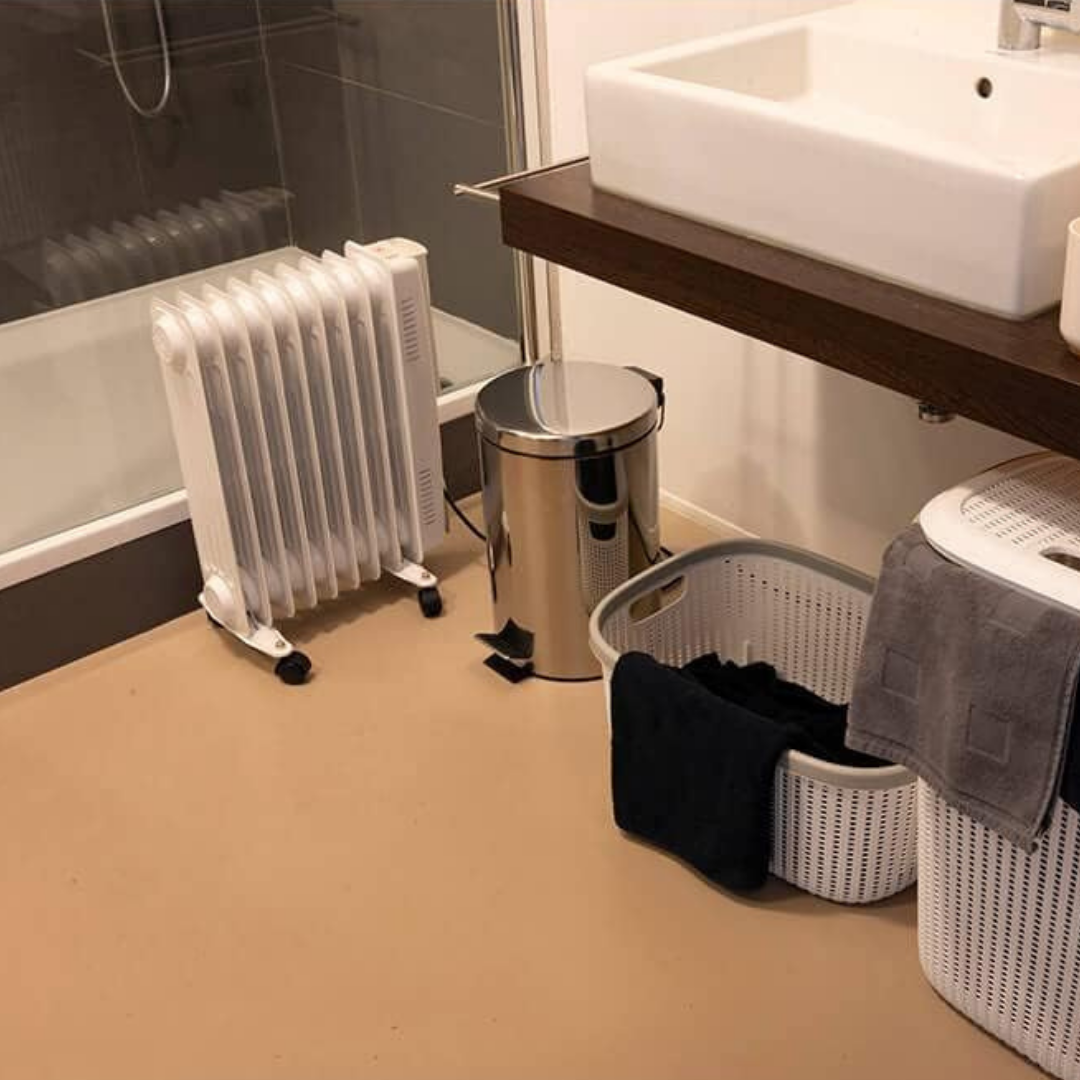 Ein weißer Ölofen steht neben einer Badewanne, daneben ein Mülleimer und Wäschekörbe.