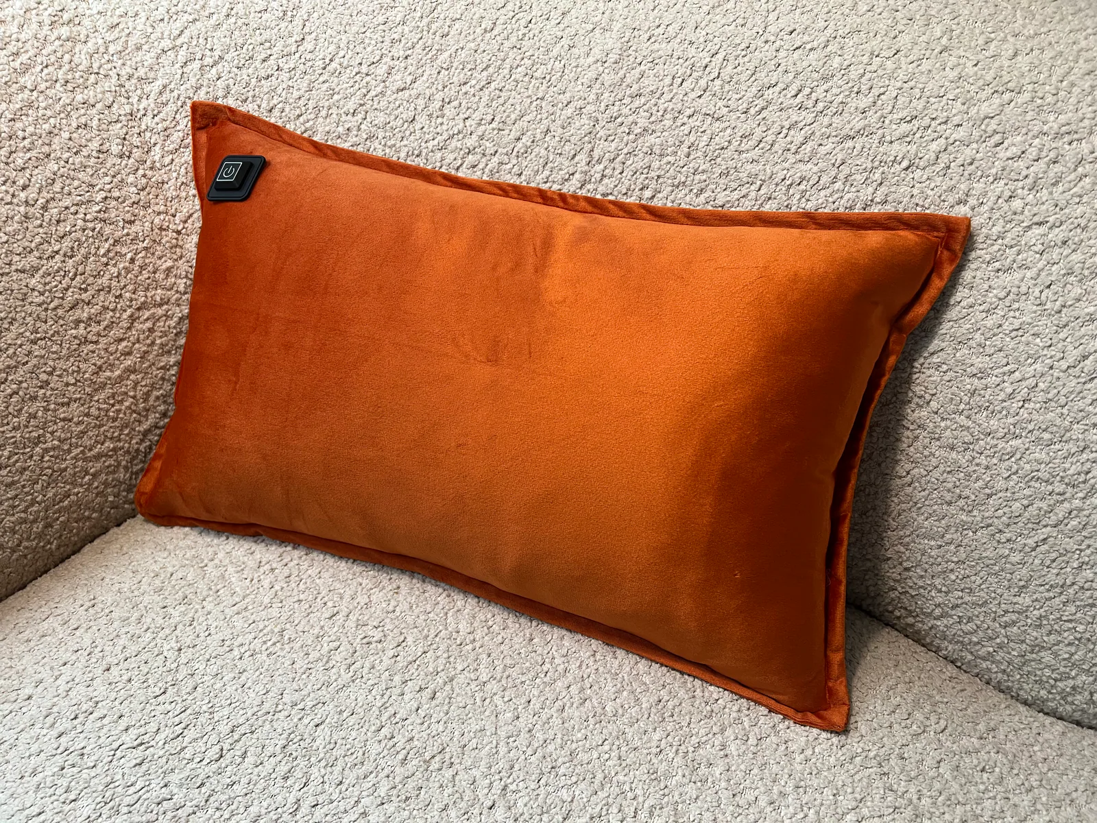 Ein orangefarbenes Kissen mit einem schwarzen Ein/Aus-Symbol liegt auf einem hellgrauen Sofa.