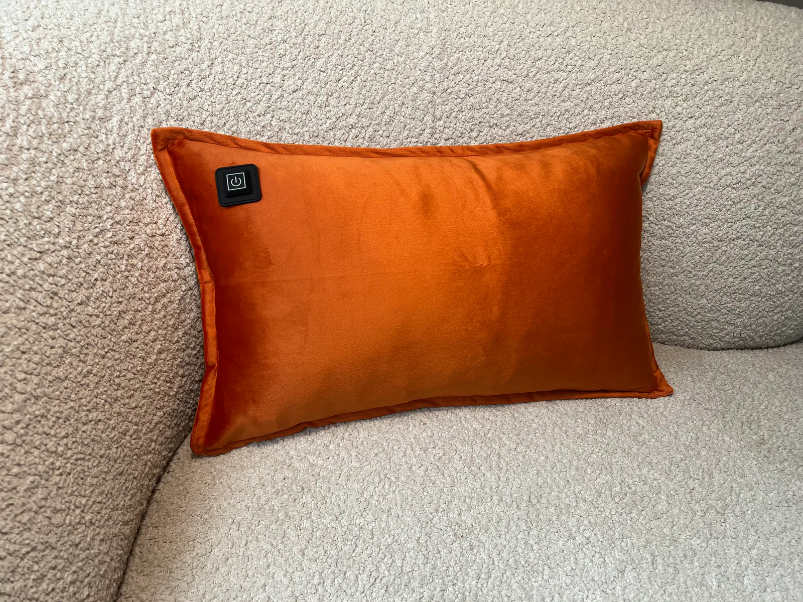 Ein orangefarbenes Kissen mit einem schwarzen Netzschalter liegt auf einem hellgrauen Sofa.