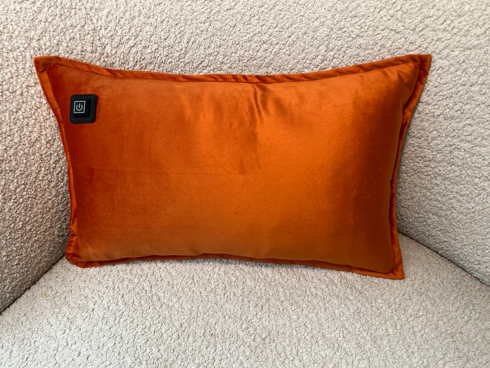 Ein orangefarbenes Kissen mit einem schwarzen Power-Symbol-Schalter liegt auf einem hellgrauen, texturierten Stuhl.