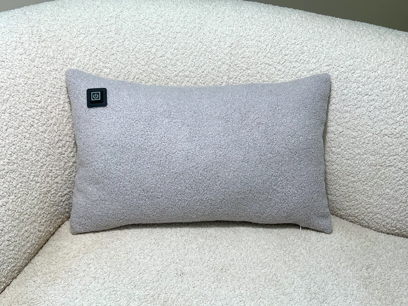 Graues Kissen mit schwarzem Power-Symbol auf cremefarbenem Bouclé-Sofa.