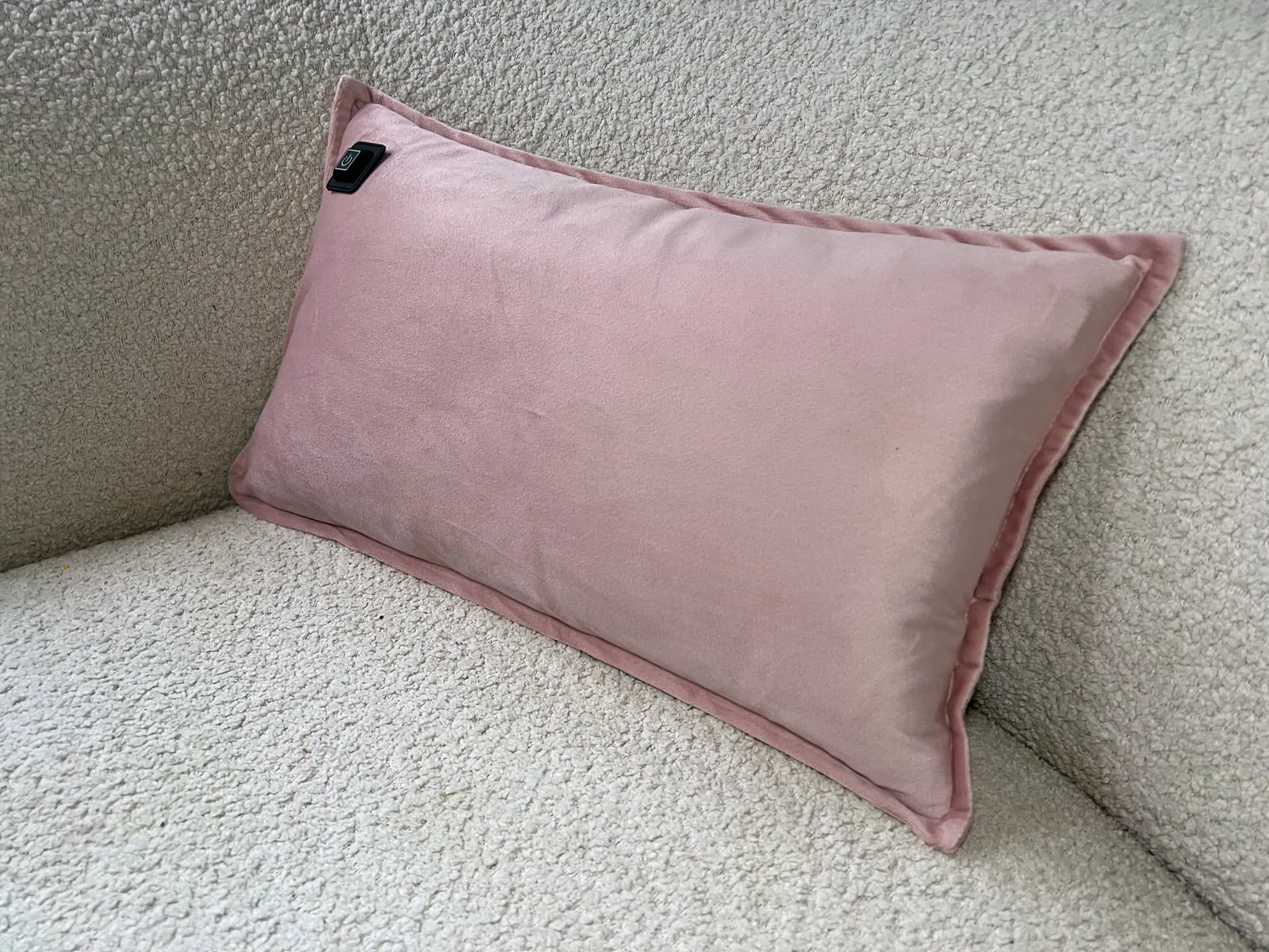Ein rosa Kissen mit schwarzem Etikett liegt auf einem cremefarbenen, flauschigen Sofa.
