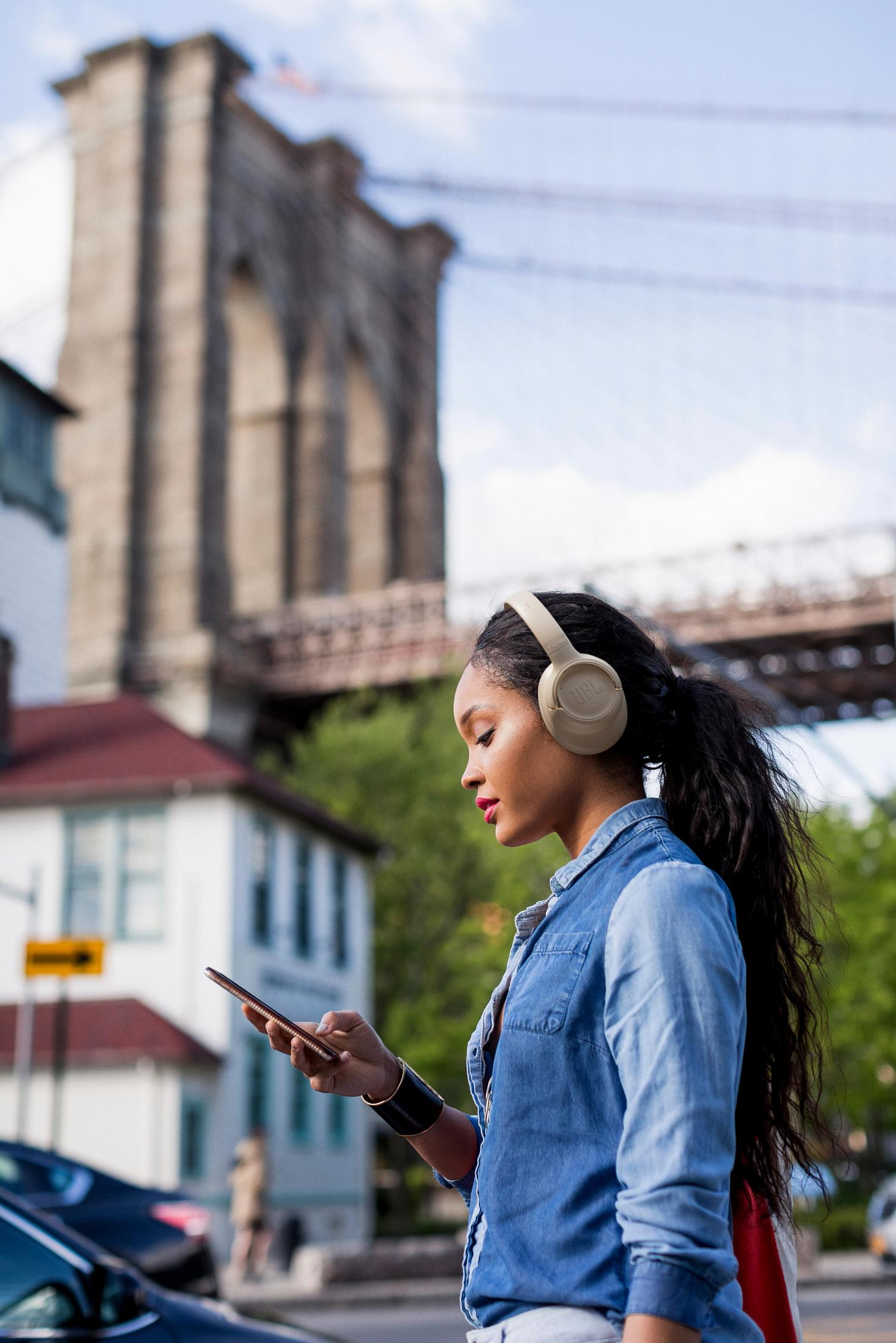 Woman with headphones and phone in front of the Brooklyn Bridge.