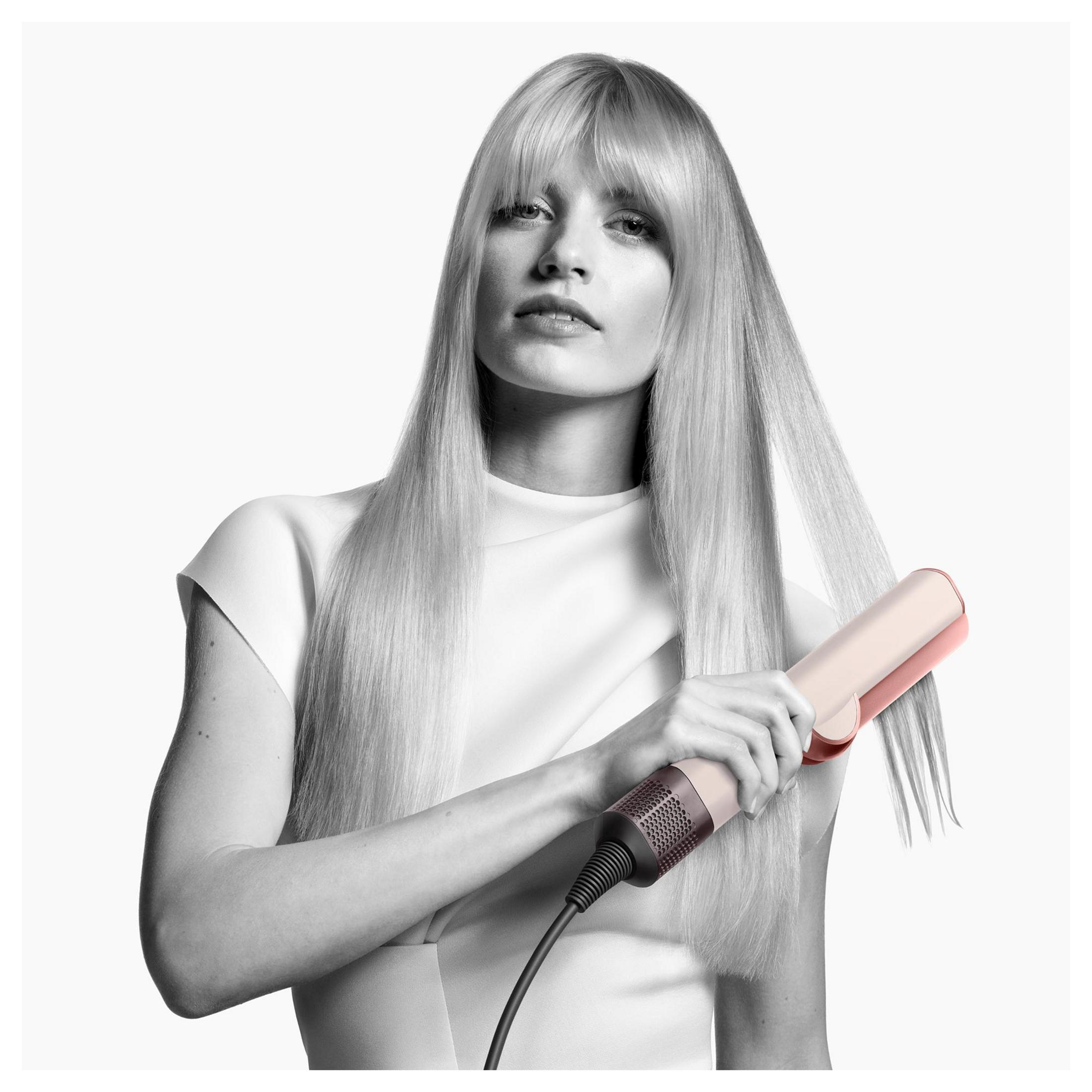 Donna con lunghi capelli biondi si liscia i capelli con una piastra rosa.