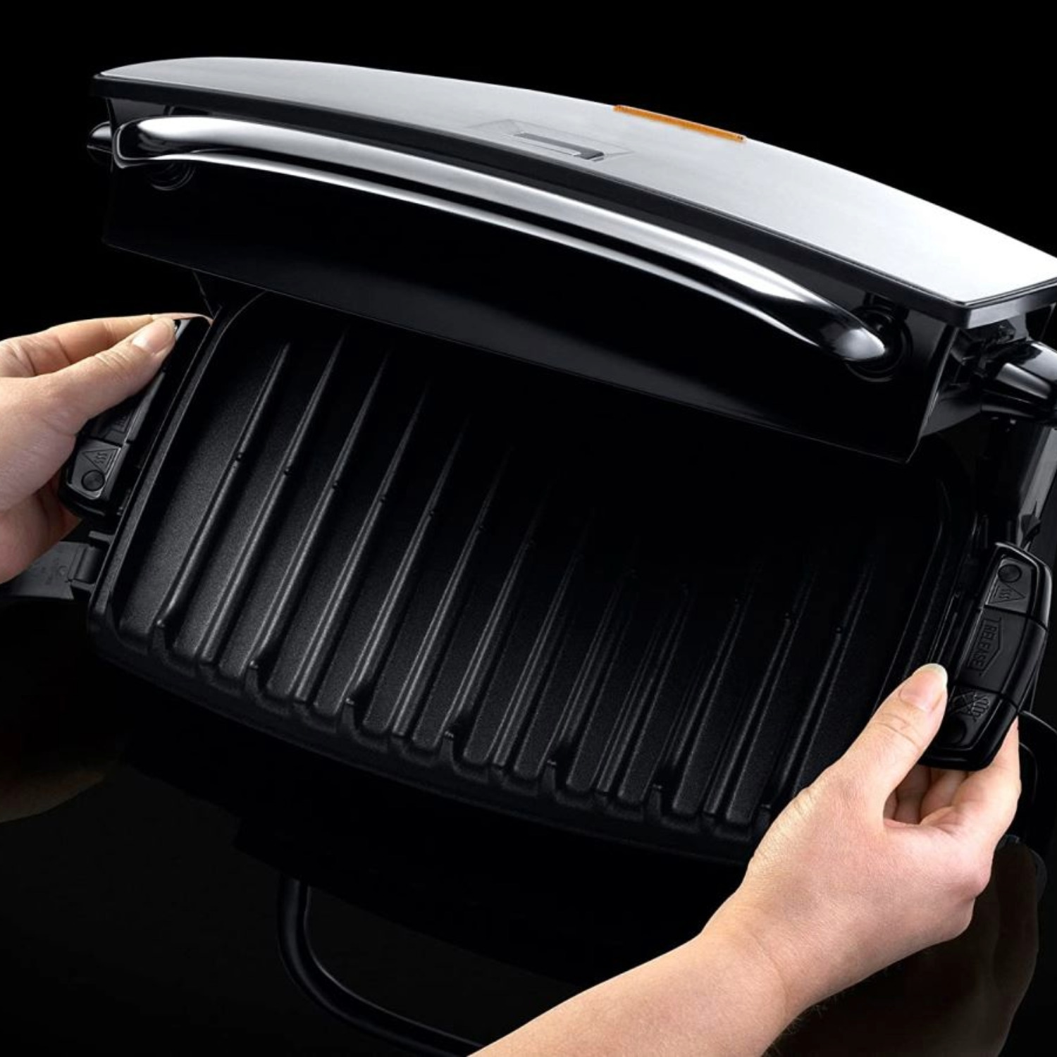 Ein schwarzer Elektrogrill mit geriffelten Platten wird von Händen geöffnet.