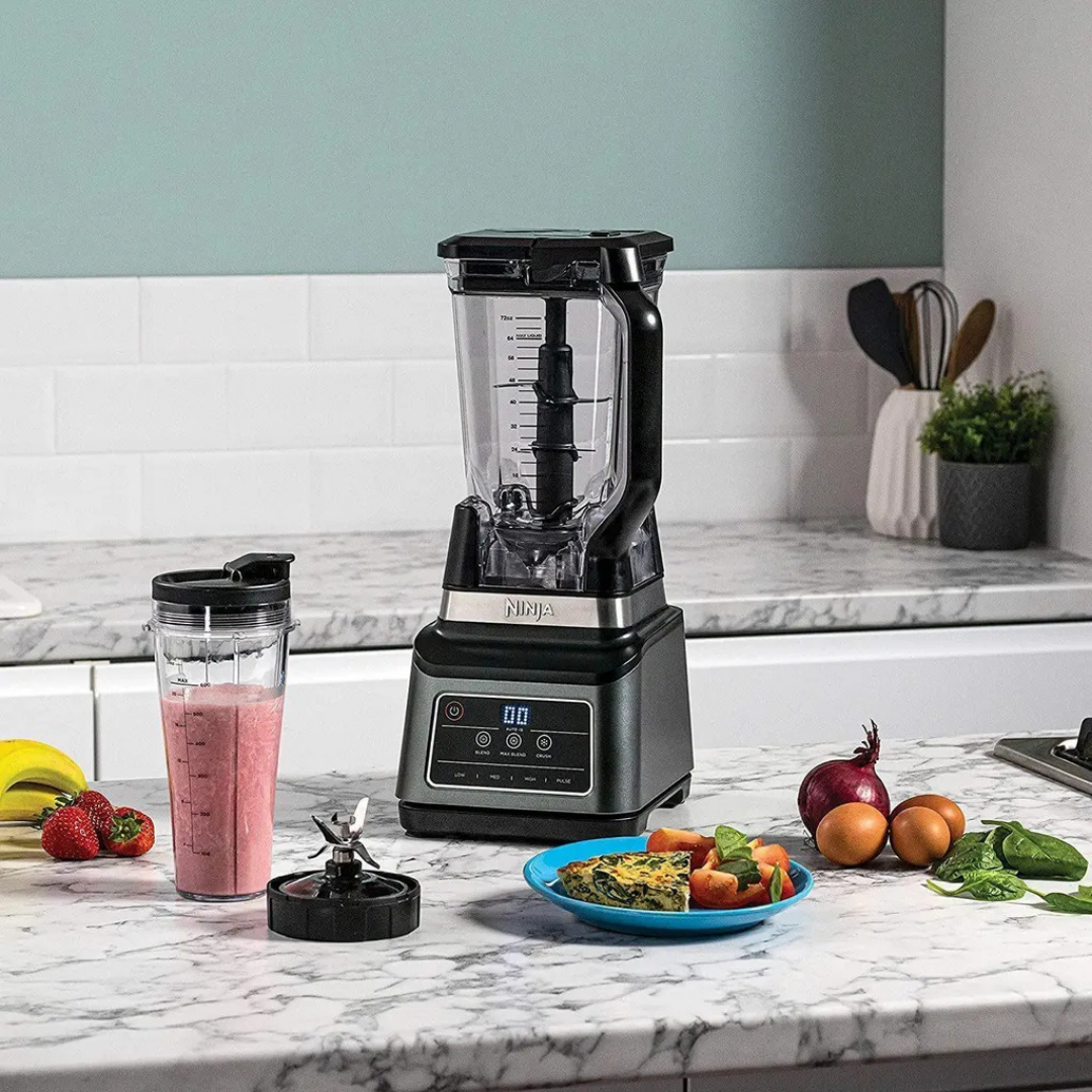 Ein Ninja-Mixer steht auf einer Marmorküchenarbeitsplatte mit Zutaten.