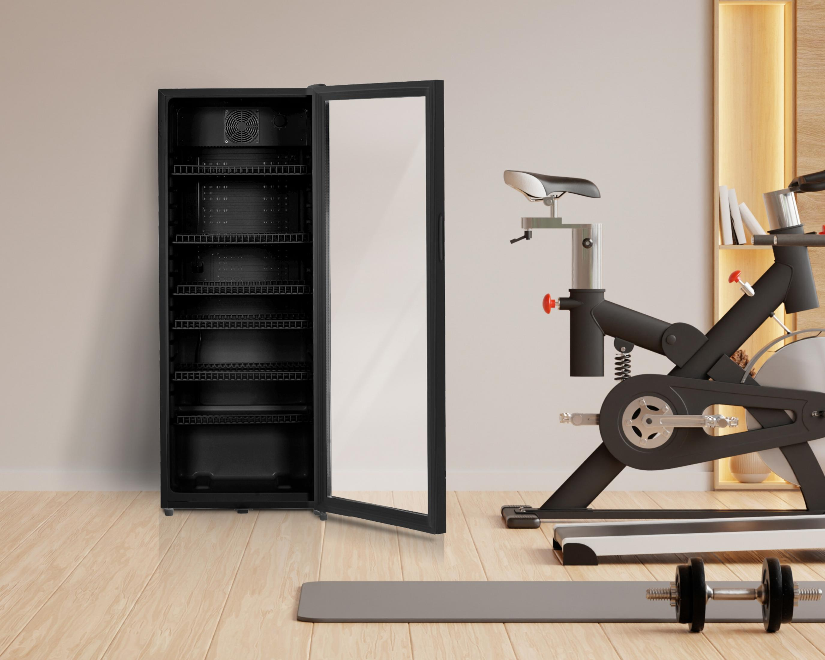 Ein schwarzer Kühlschrank mit offener Tür neben einem Heimtrainer, Hanteln und Matte.