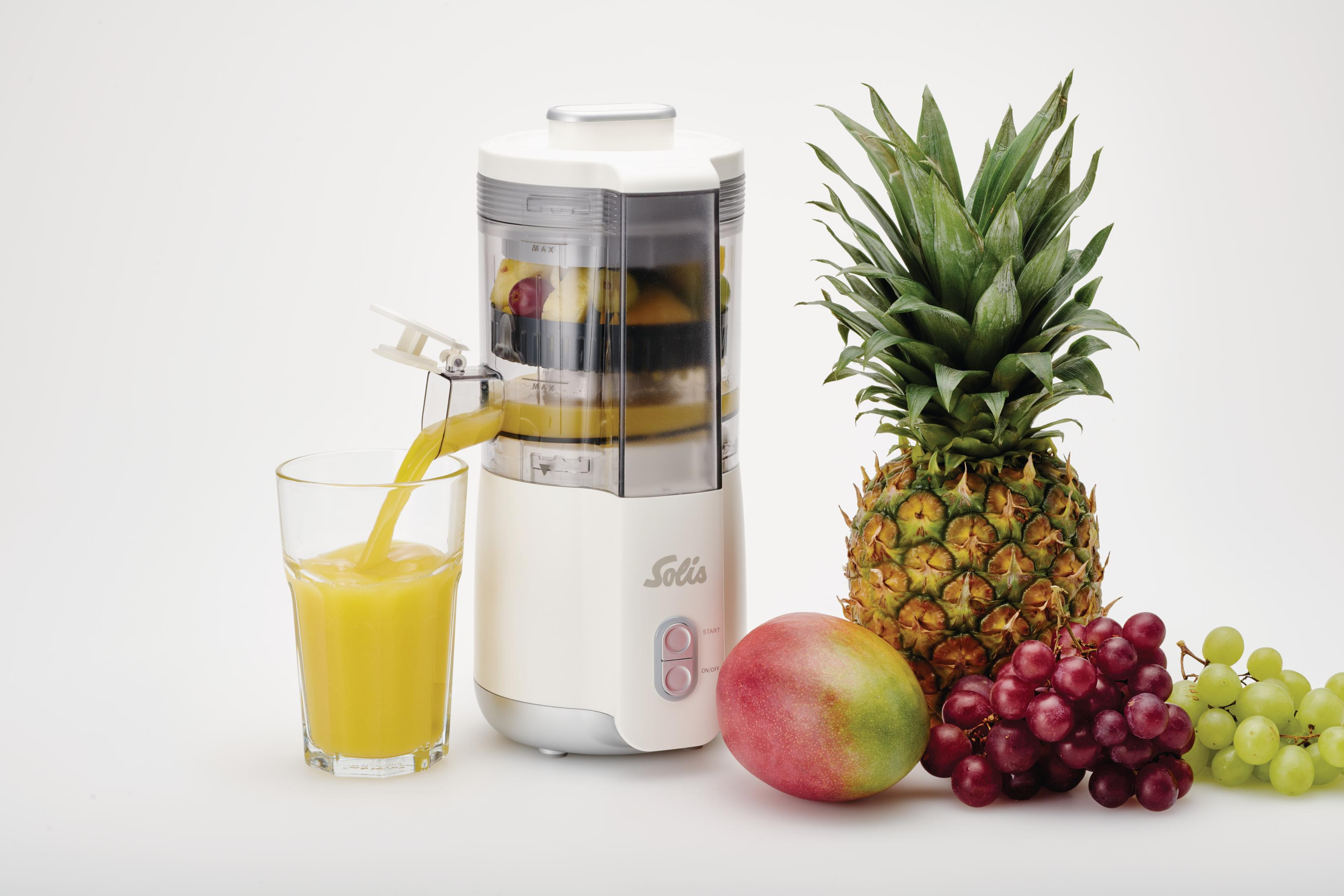 Un estrattore versa succo in un bicchiere, accanto a frutta come ananas, mango e uva.