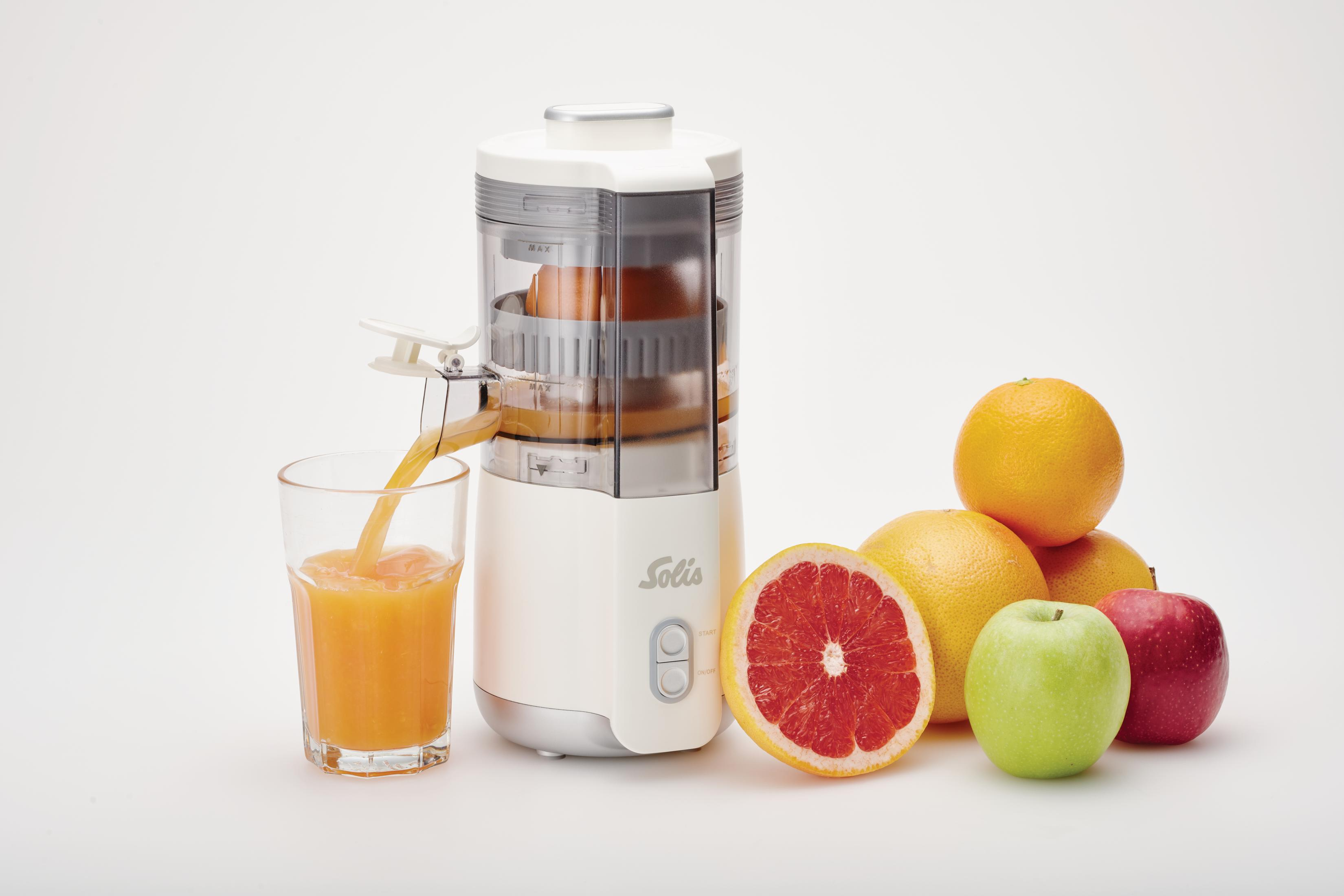 Un estrattore immette succo in un bicchiere, con frutta accanto.