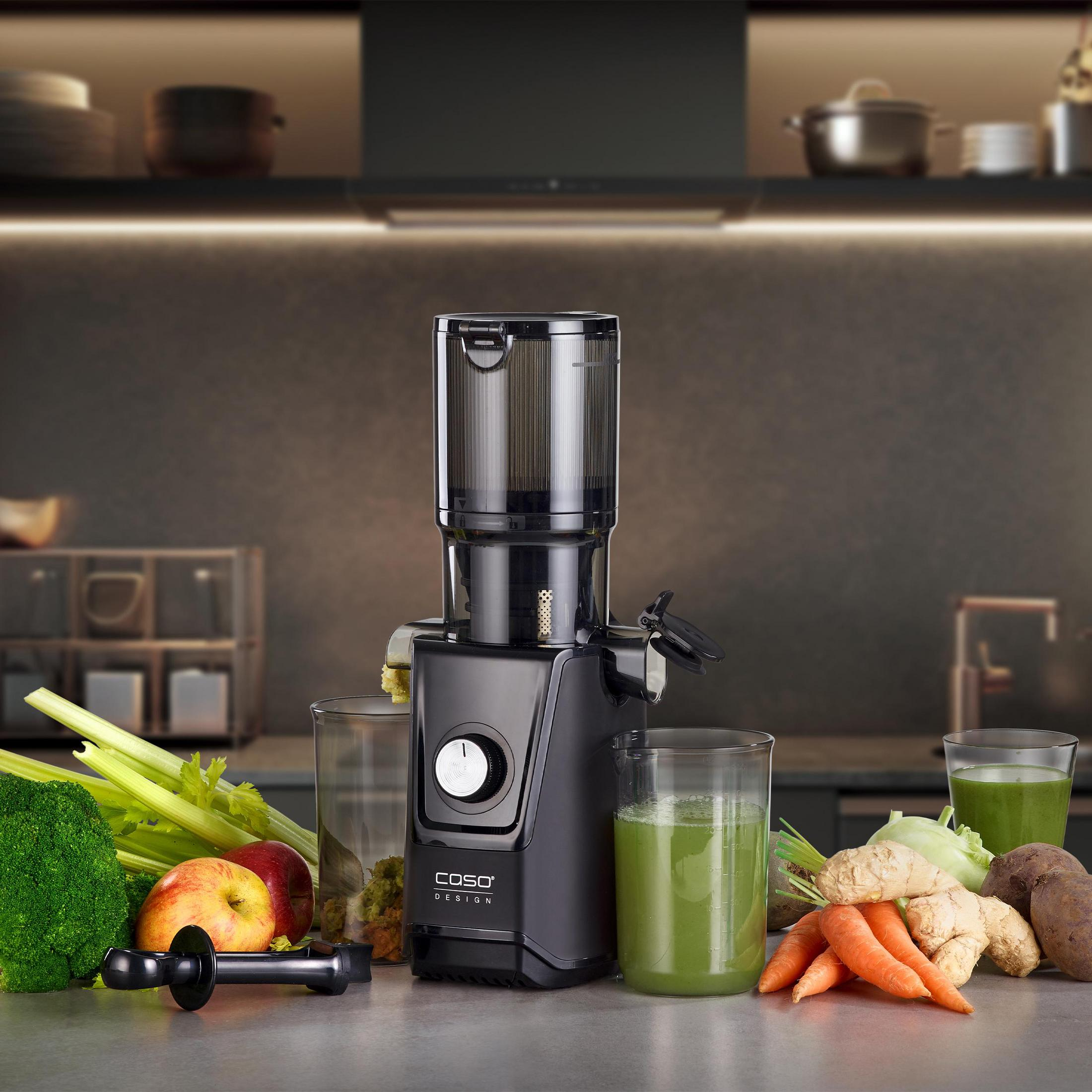 Un estrattore di succo nero su un bancone con verdure fresche e succhi intorno.