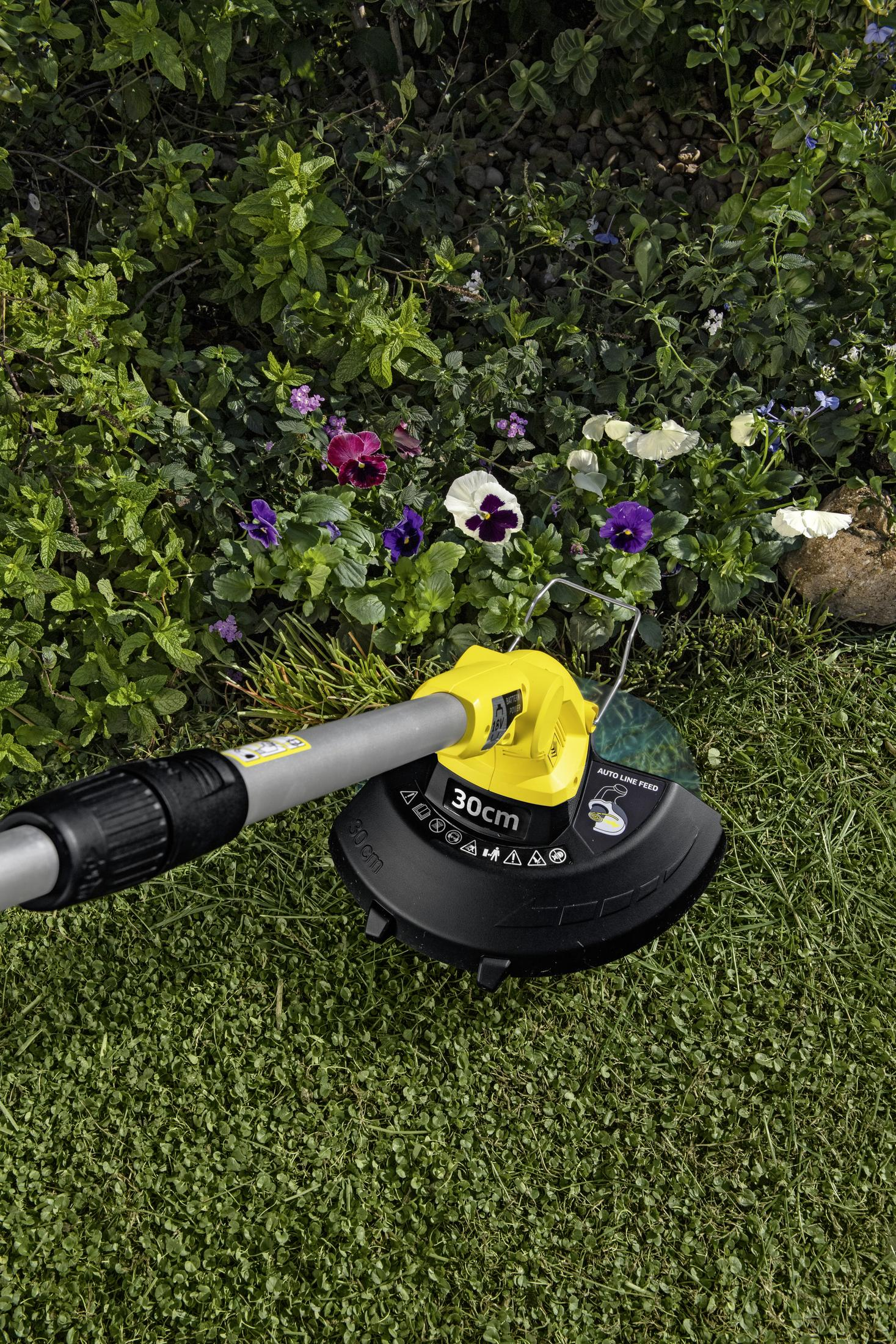 Ein gelber Rasentrimmer liegt auf einem Rasen mit Blumen und Grünpflanzen.