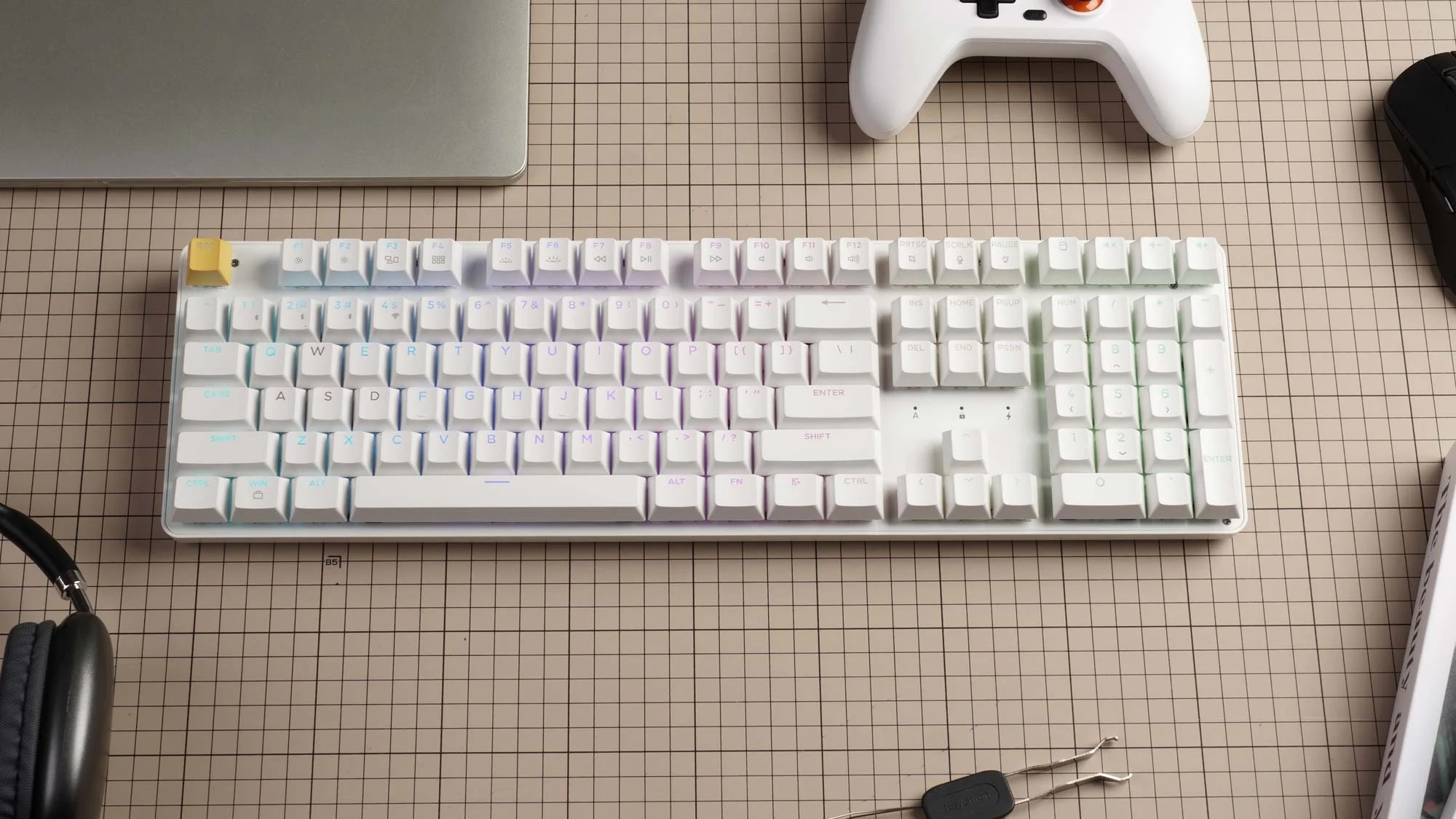 Biała klawiatura mechaniczna z podświetleniem RGB, laptop, słuchawki, mysz i kontroler.