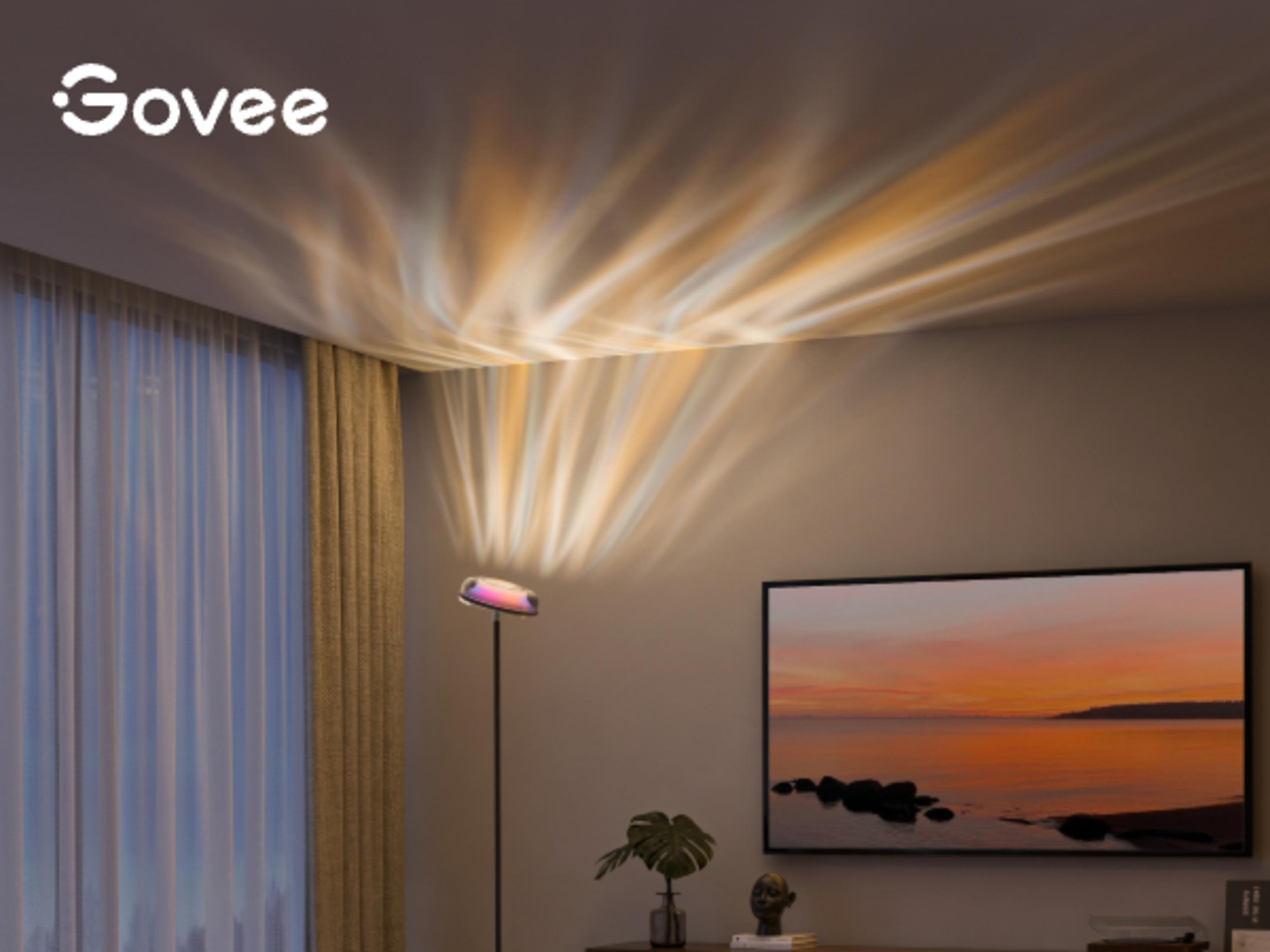 Un proiettore a piantana proietta motivi colorati su soffitto e parete sopra un TV.