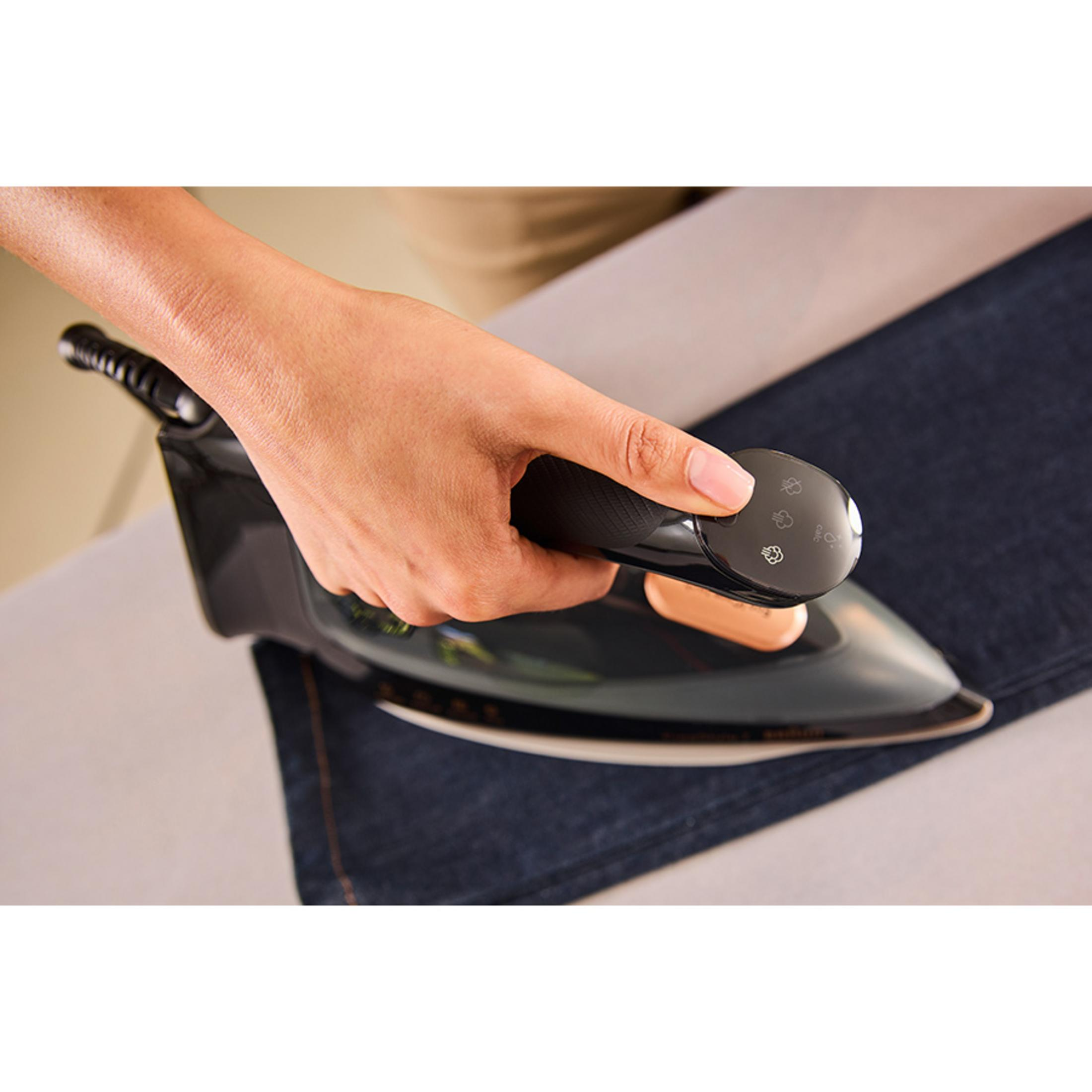 Una mano tiene un ferro da stiro nero che scivola su tessuto di jeans blu scuro.