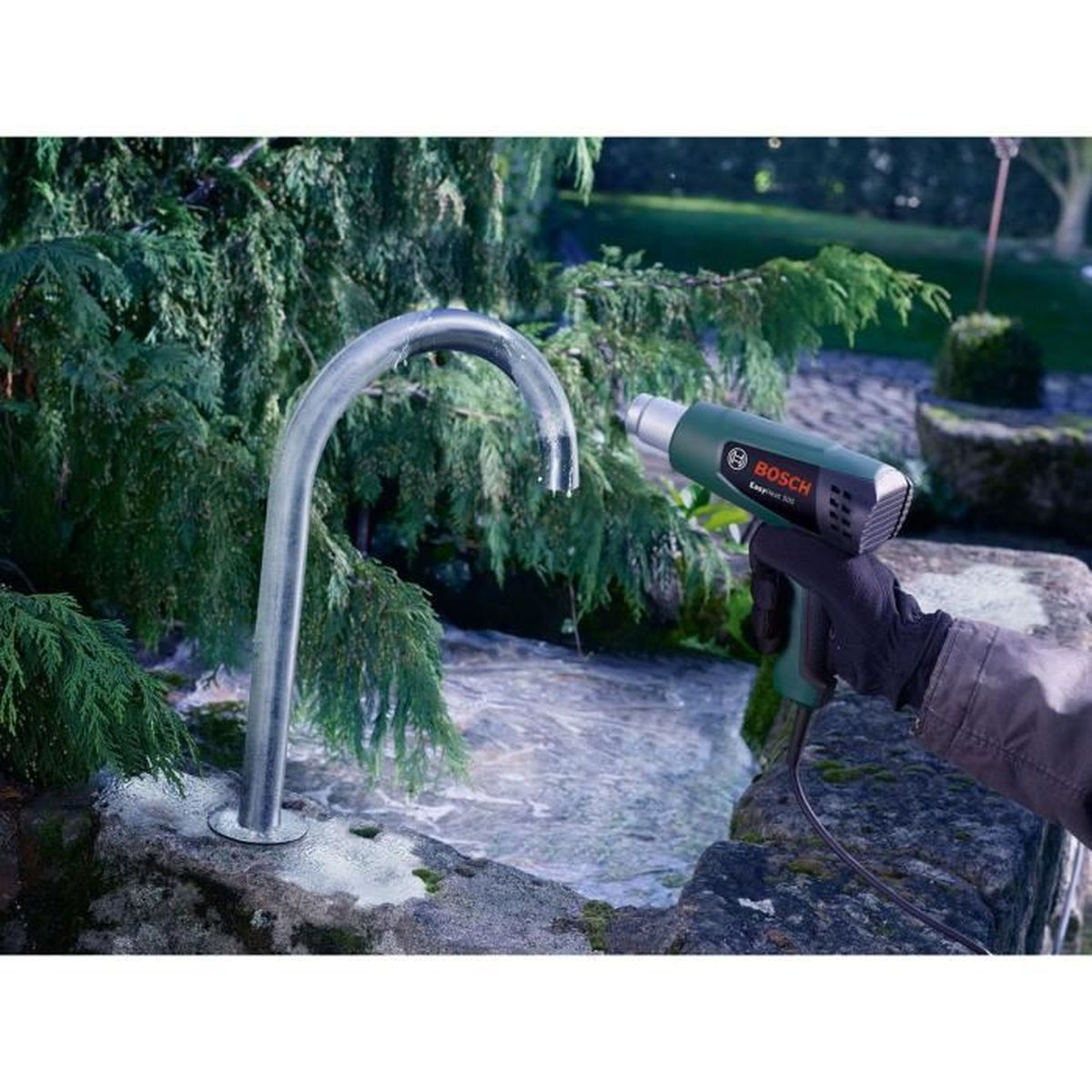 Eine Hand hält eine grüne Bosch-Heißluftpistole in der Nähe eines gefrorenen Wasserhahns.