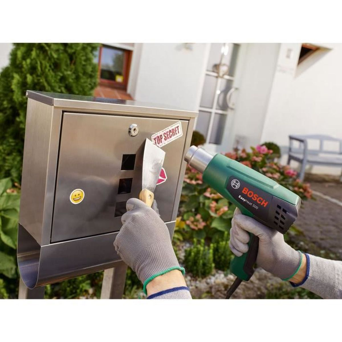 Person entfernt Aufkleber mit Heißluftpistole und Schaber von Briefkasten.