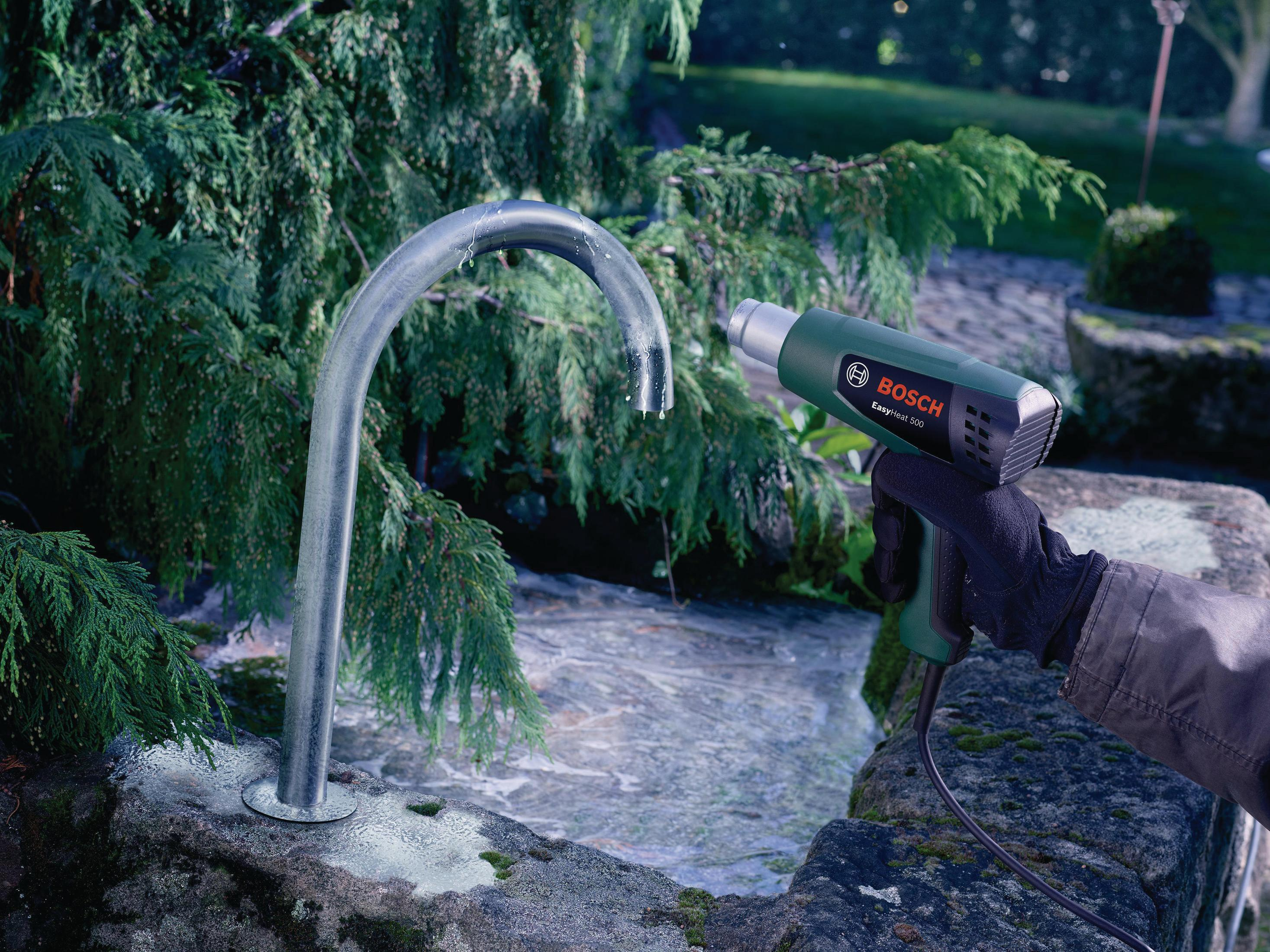 Ein grünes Bosch Heißluftgebläse wird zum Auftauen eines Rohrs mit Wasser verwendet.