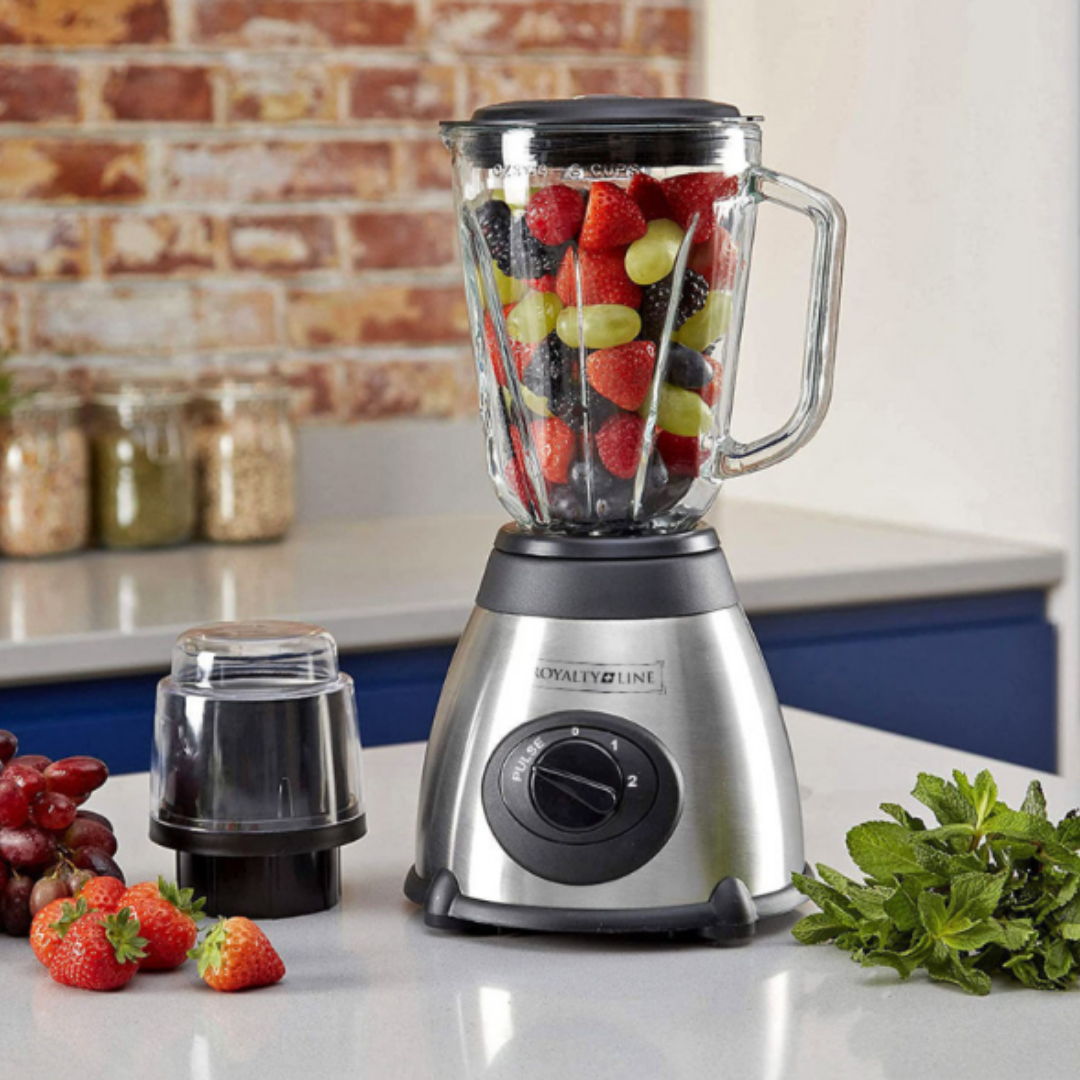 Ein Mixer gefüllt mit Beeren und Trauben steht auf einer Arbeitsplatte neben Obst.