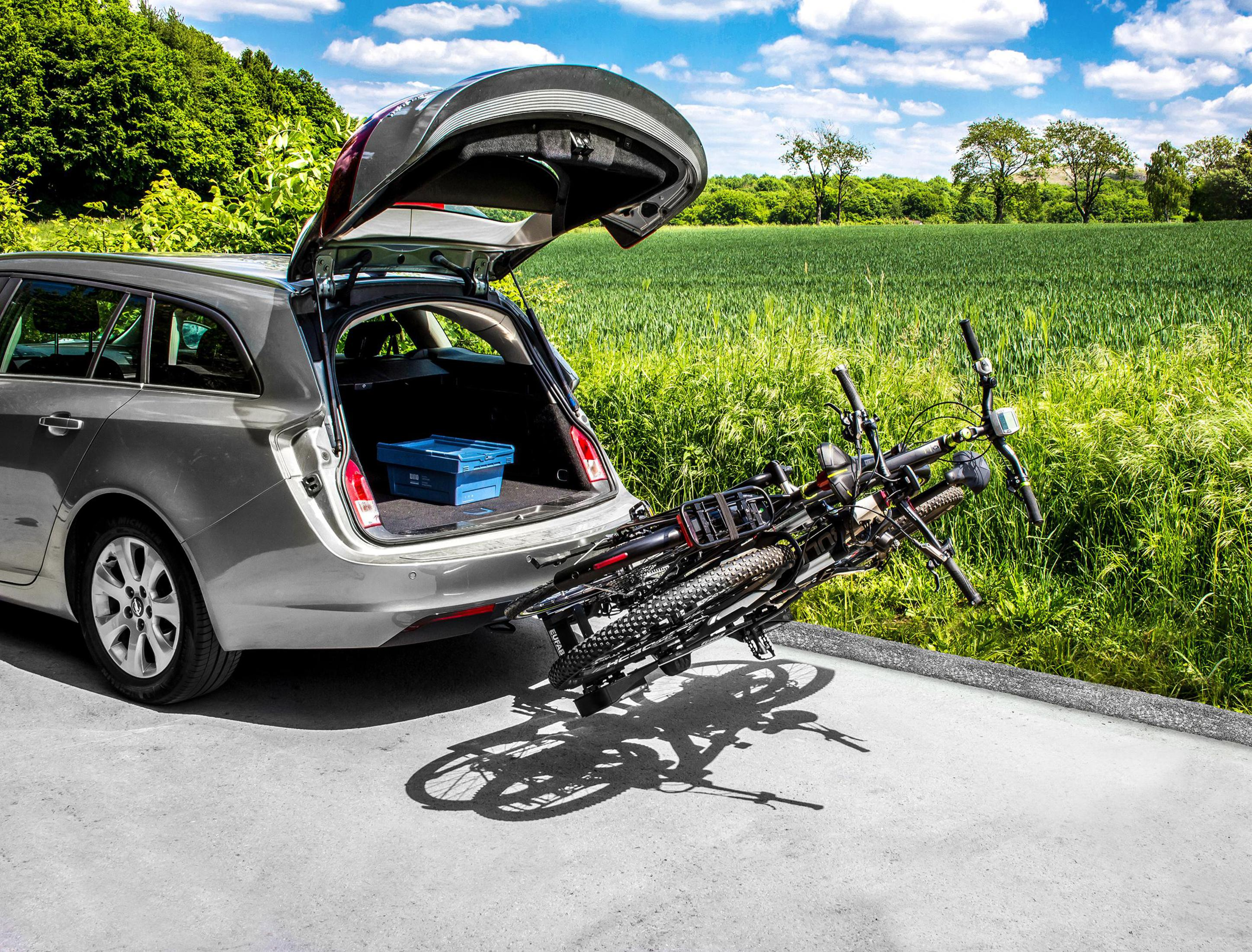 Un'auto argento con baule aperto, carica di biciclette, parcheggiata sull'asfalto.