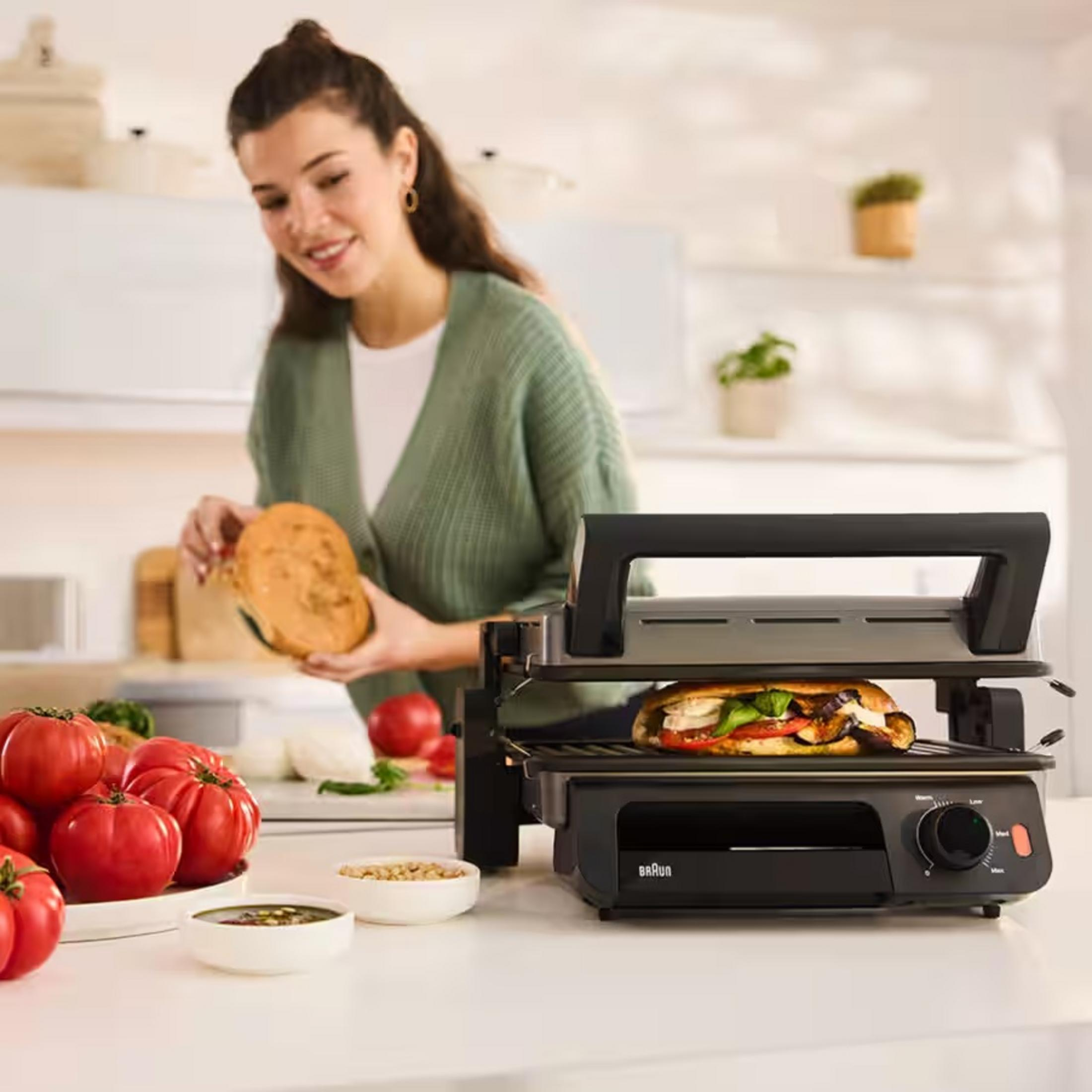 Frau bereitet Sandwich zu, Tomaten und Panini-Grill auf Küchentheke.