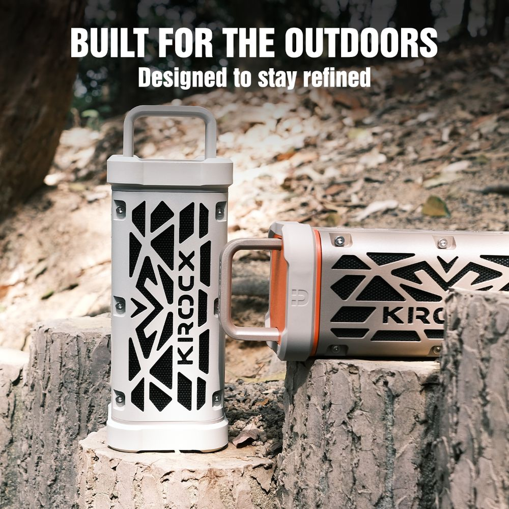 Dos altavoces KROCX para exteriores, uno blanco y uno bronce, sobre troncos. Texto: "BUILT FOR THE OUTDOORS."