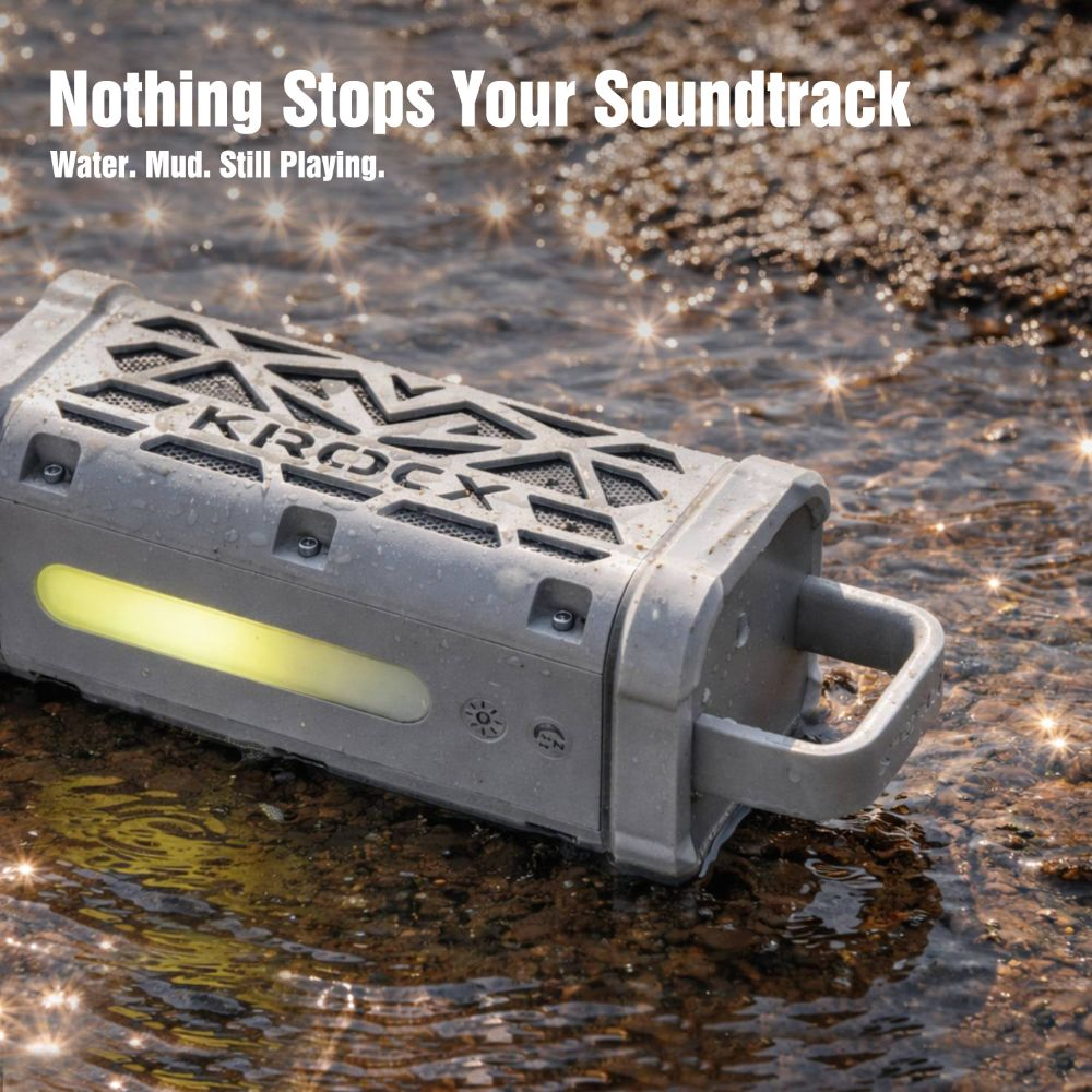 Altavoz gris e impermeable con LED amarillo en agua poco profunda sobre piedras.