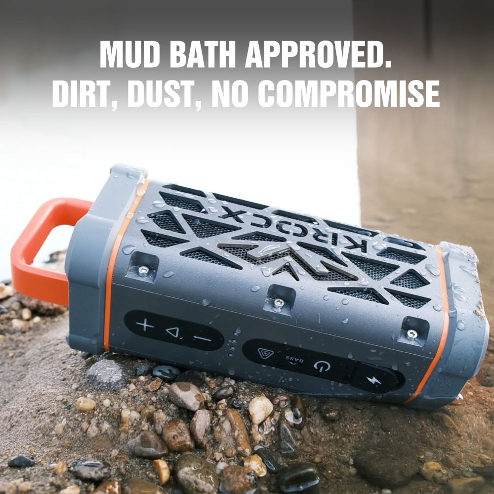 Un altavoz Bluetooth Kärcher gris con asa naranja sobre rocas.