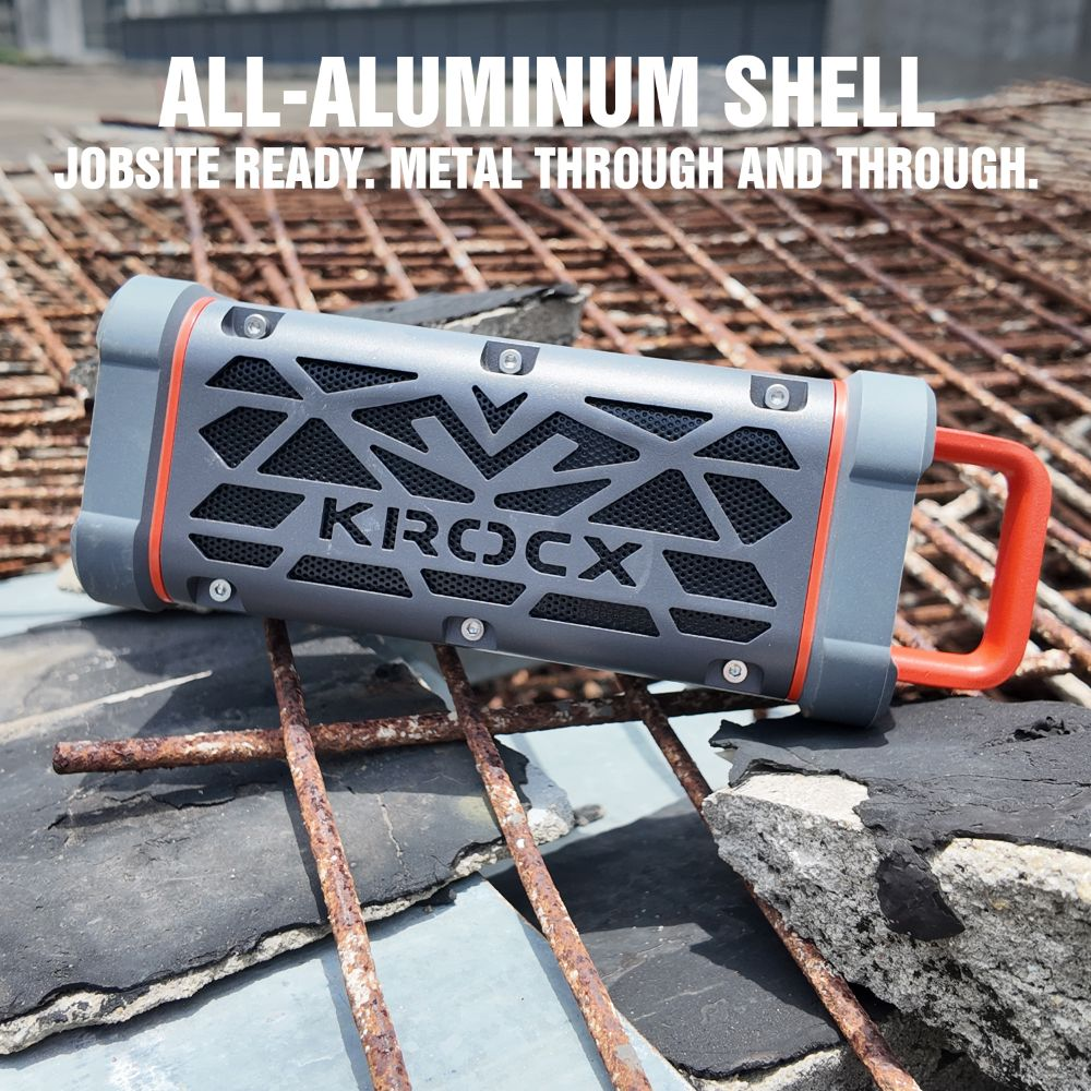 Altavoz KROCX gris con asas naranjas sobre soportes metálicos oxidados.