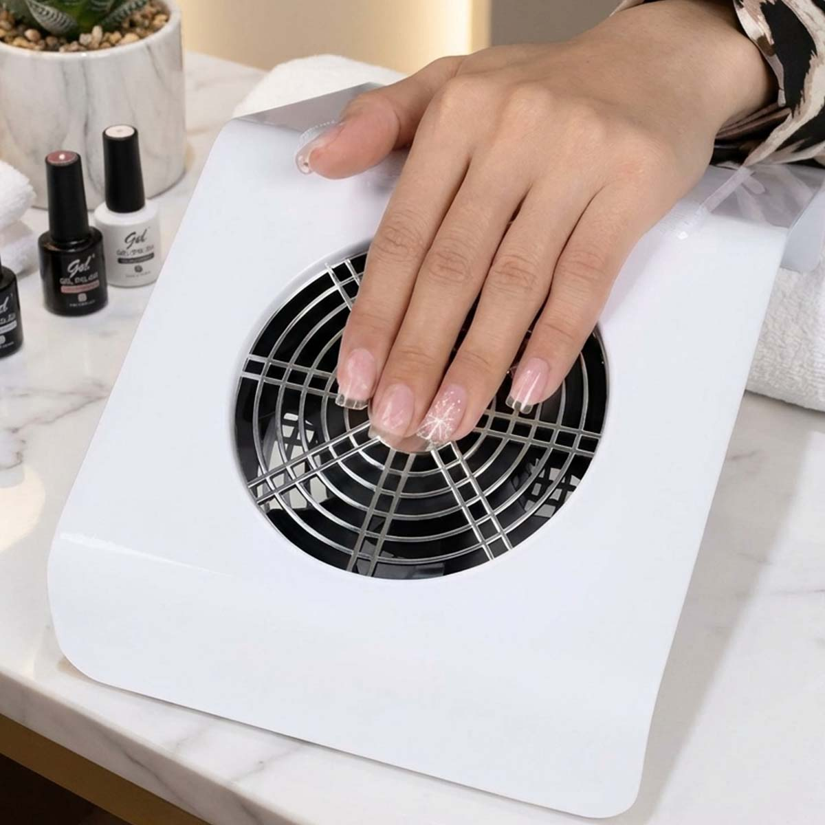 Eine Hand mit klaren Nägeln ruht über einem weißen Nagellüfter.