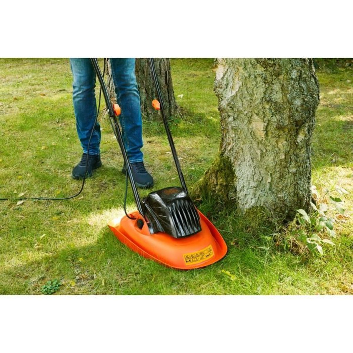 Person mäht Gras mit einem orangefarbenen Rasenmäher neben einem Baum.