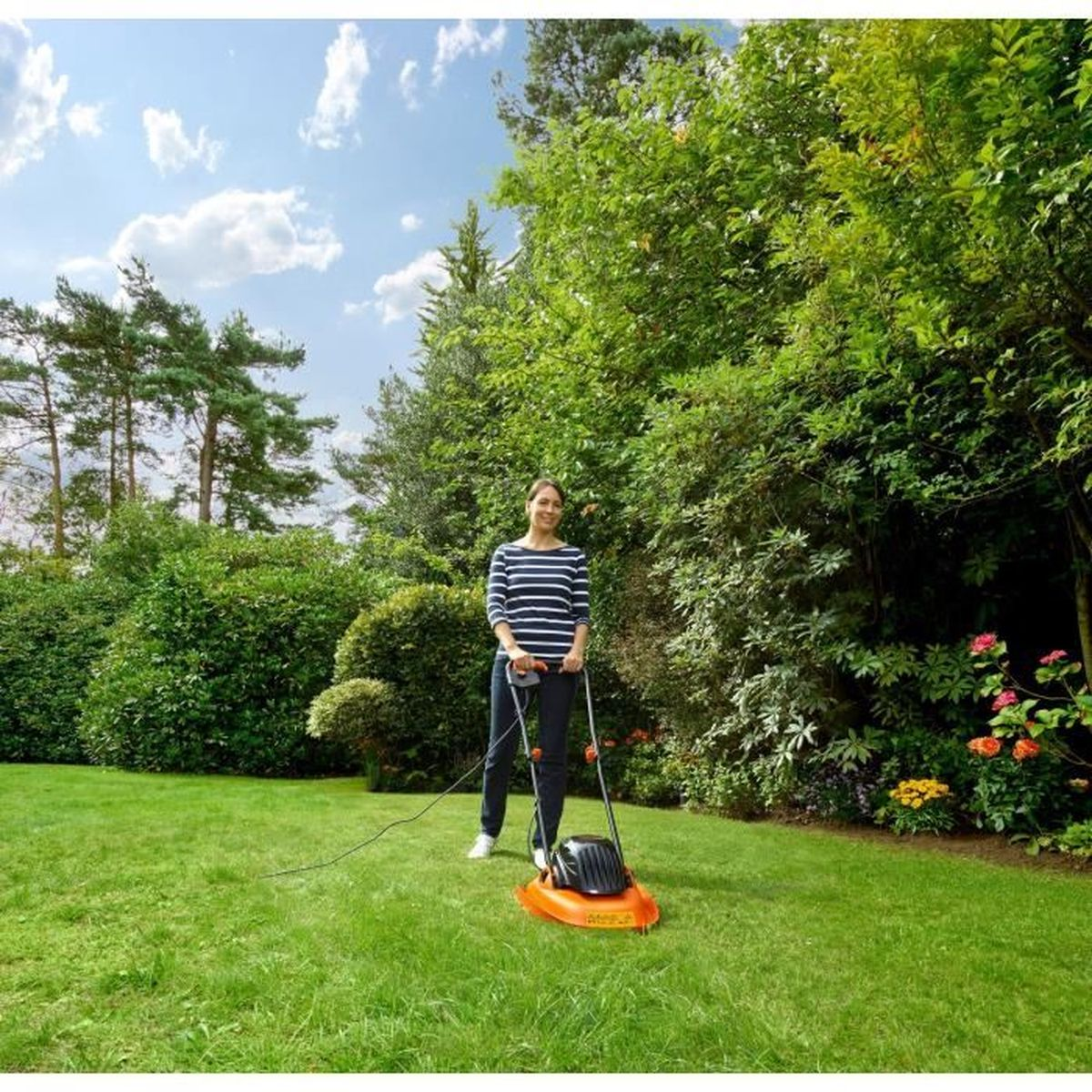 Eine Frau mäht mit einem orangefarbenen Rasenmäher den Rasen in einem üppigen Garten.