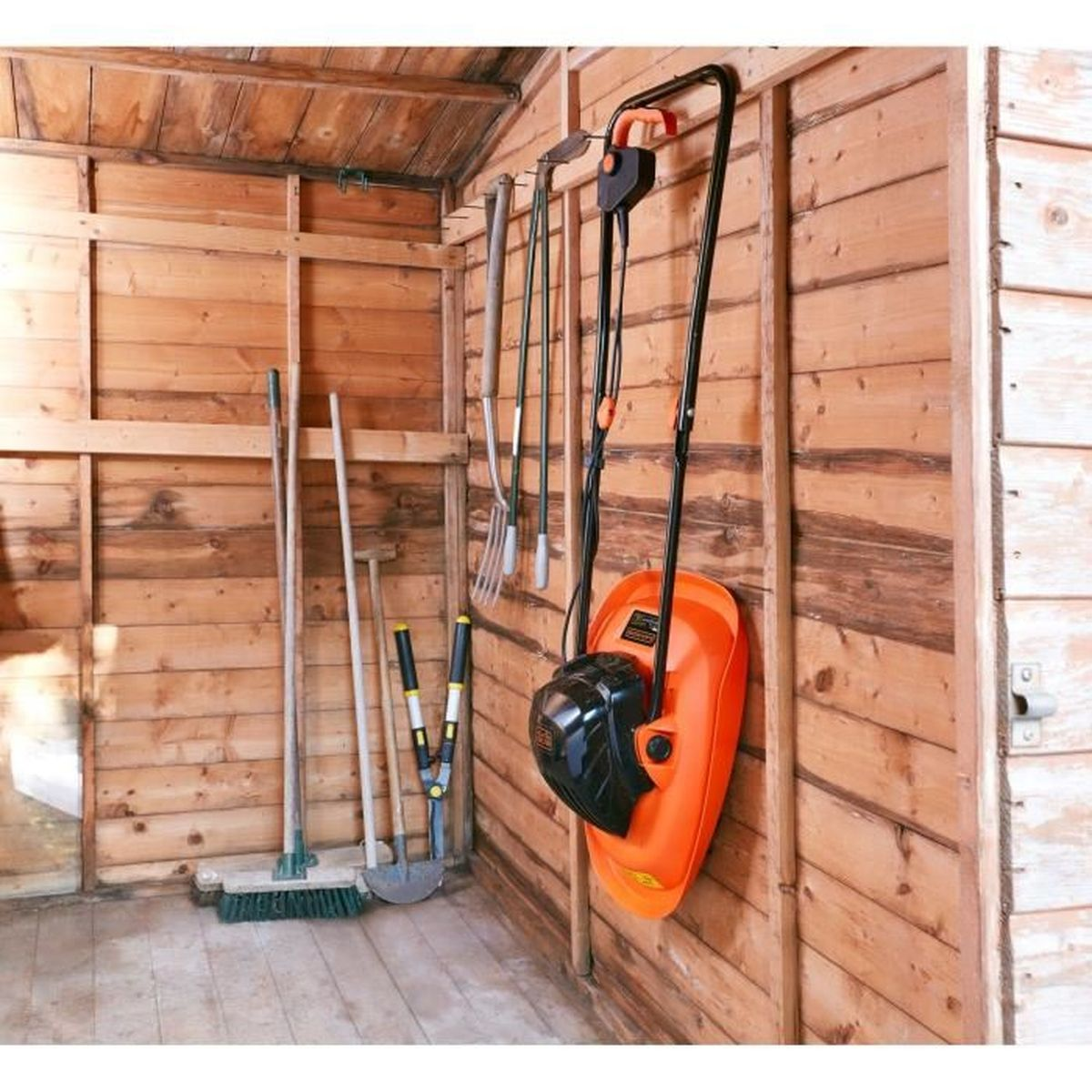 Gartenwerkzeuge und ein orangefarbener Rasenmäher hängen an der Holzwand eines Schuppens.