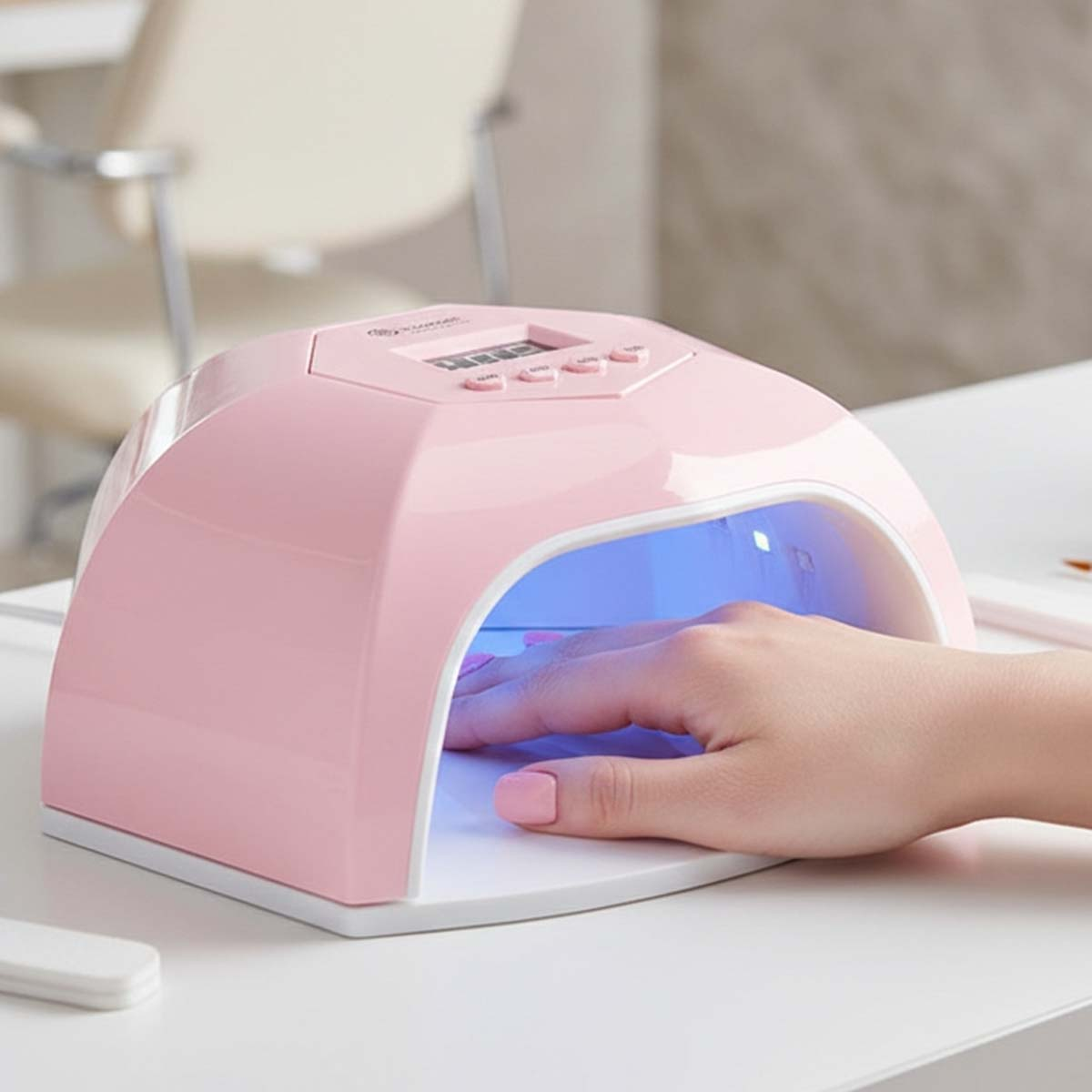 Eine Hand mit rosa lackierten Nägeln in einer rosafarbenen UV-Nagellampe.