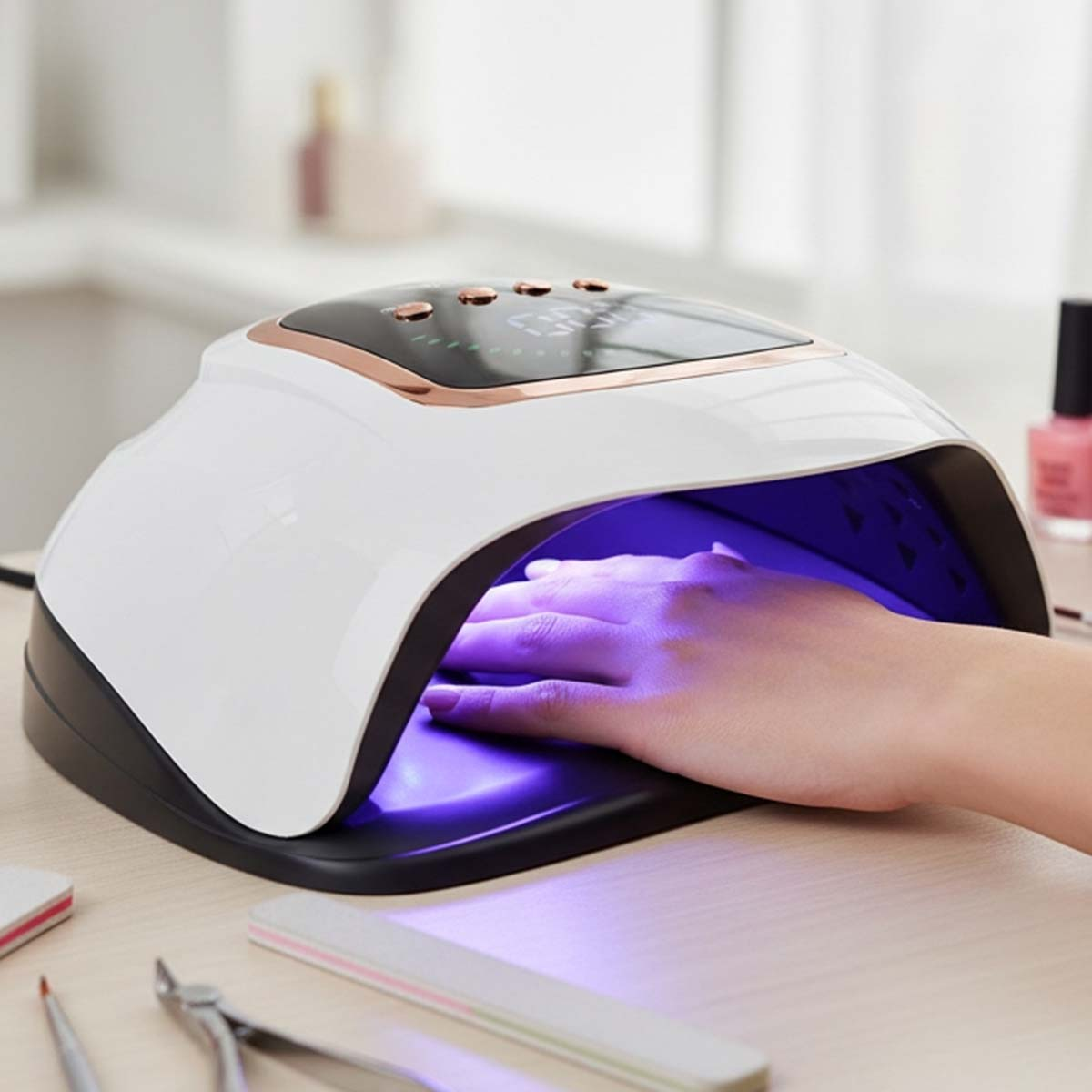 Eine Hand trocknet unter einer UV-Lampe für Nägel mit Nagellackfläschchen im Hintergrund.