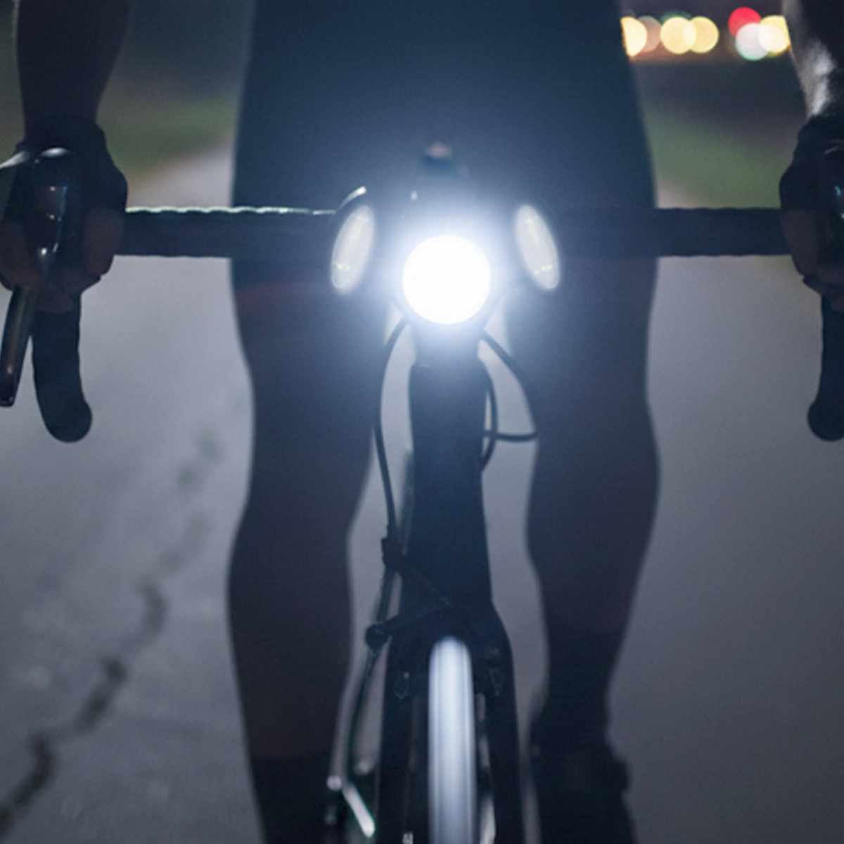 Fahrer auf einem Fahrrad mit hellem Scheinwerfer bei Nacht, Bokeh-Lichter im Hintergrund.