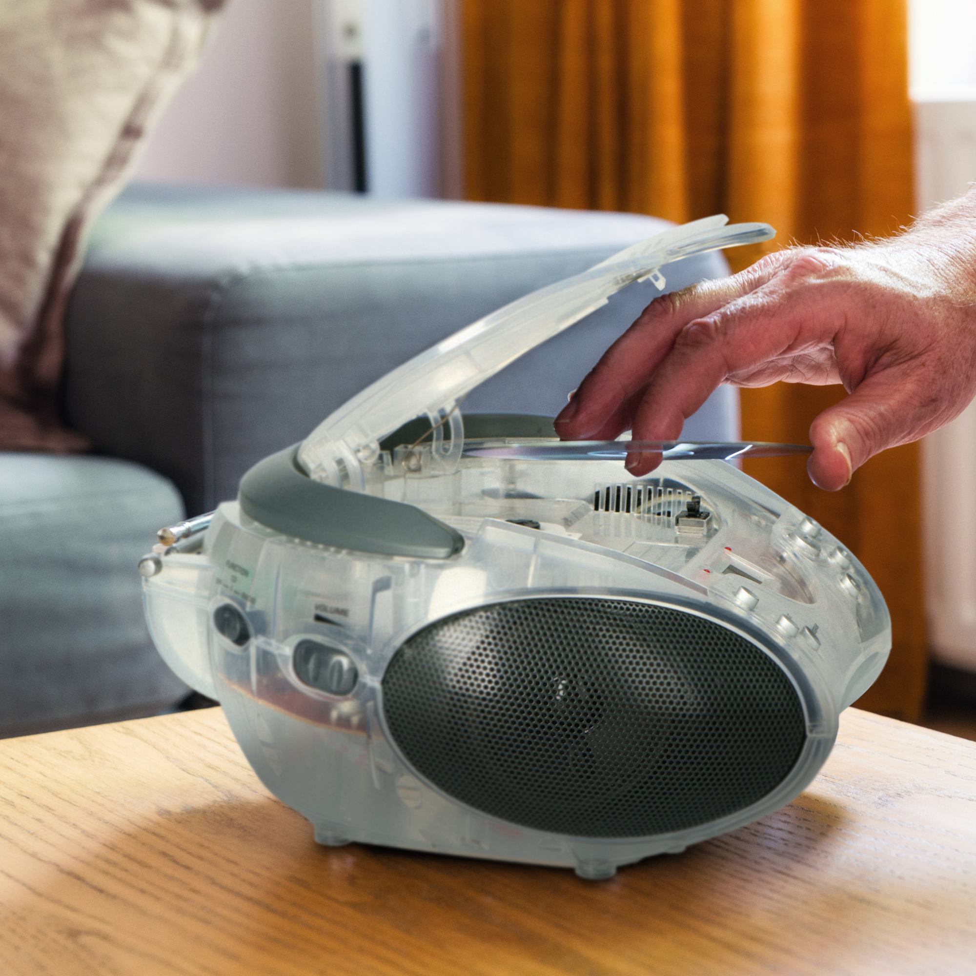 Ręka wkłada płytę CD do przezroczystego boomboxa na drewnianym stole.