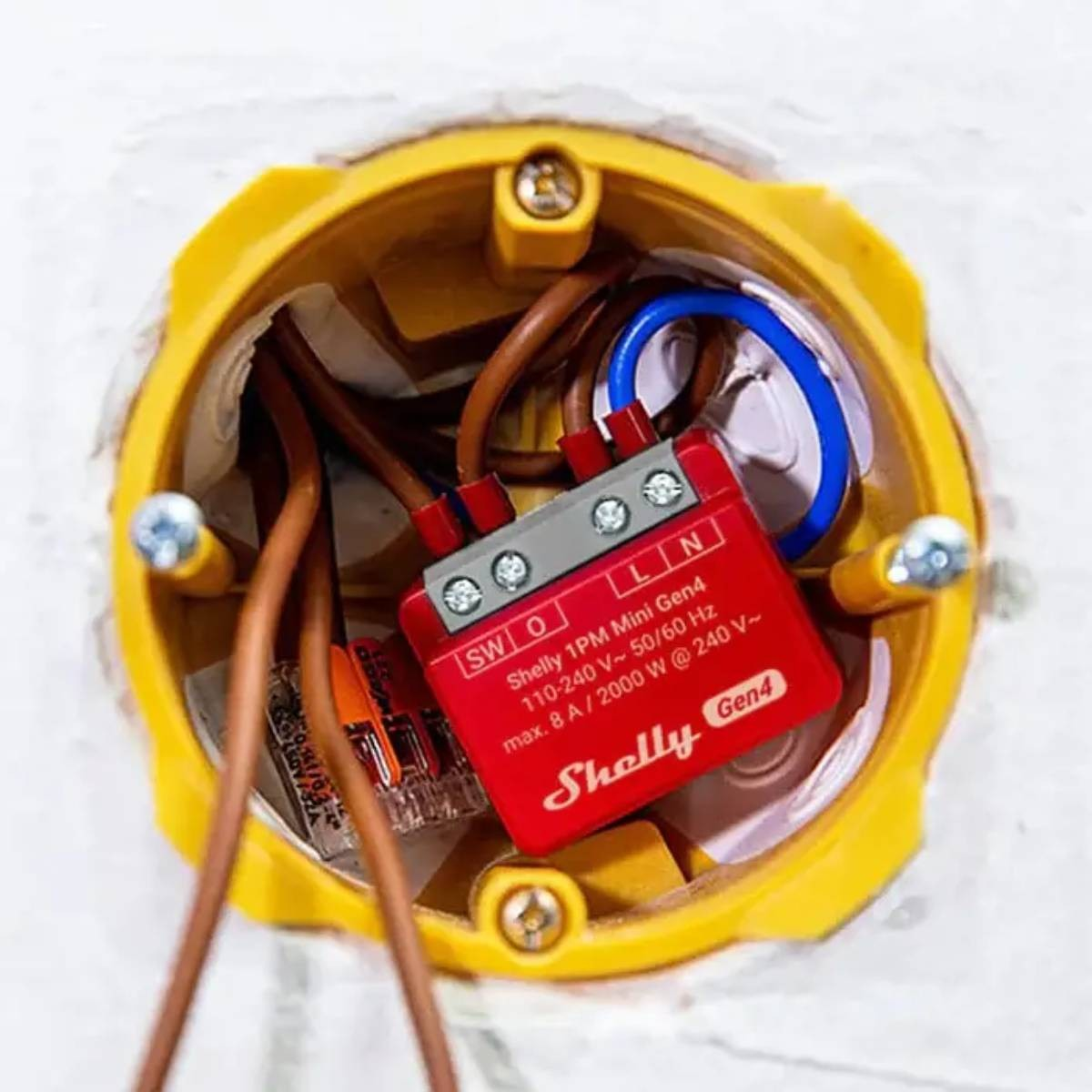 Kırmızı bir Shelly 1PM Mini Gen4 cihazı, kablolarla sarı bir elektrik kutusunun içine monte edilmiştir.