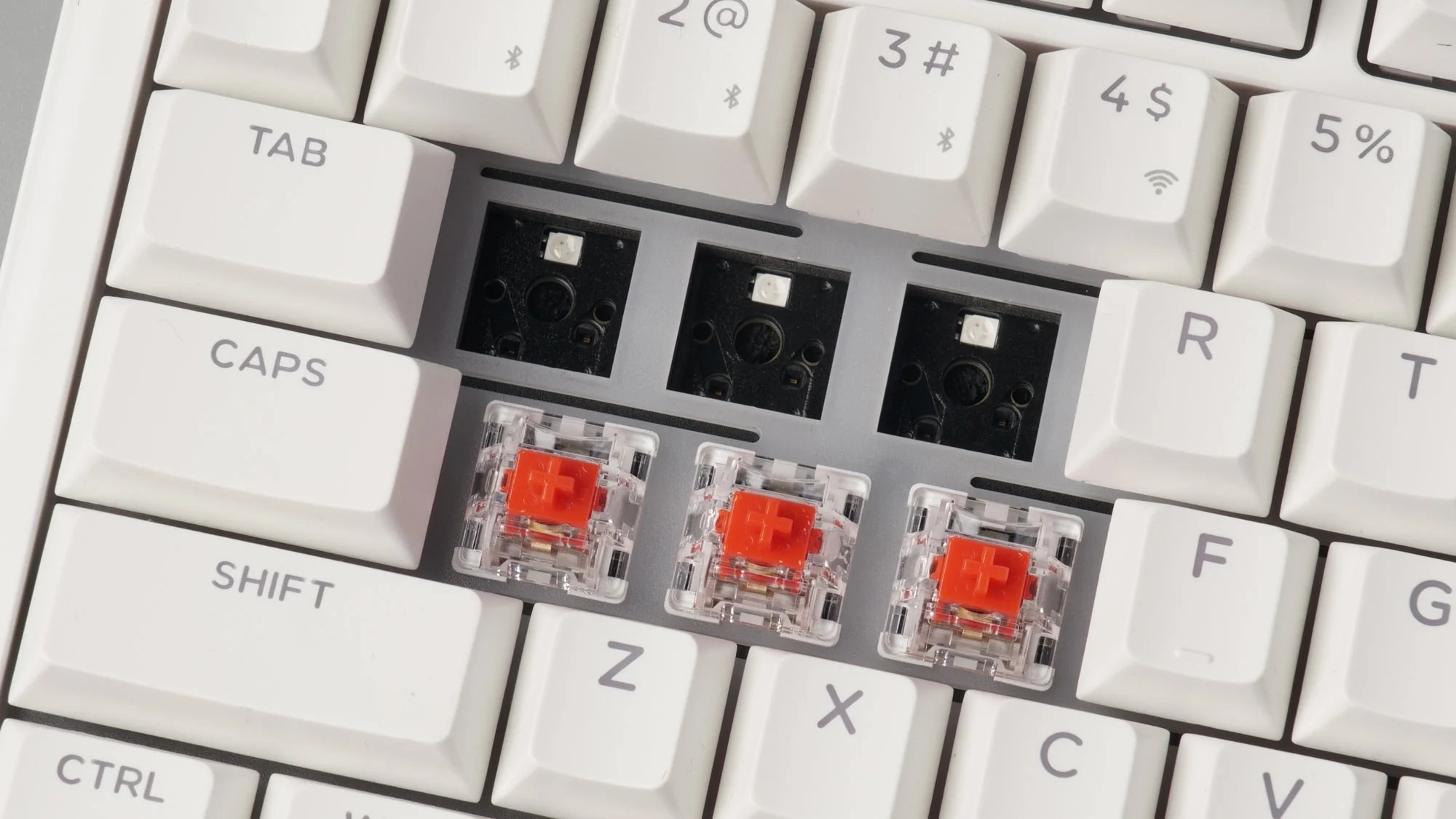 Zbliżenie białej klawiatury z trzema zainstalowanymi czerwonymi przełącznikami i pustymi miejscami.