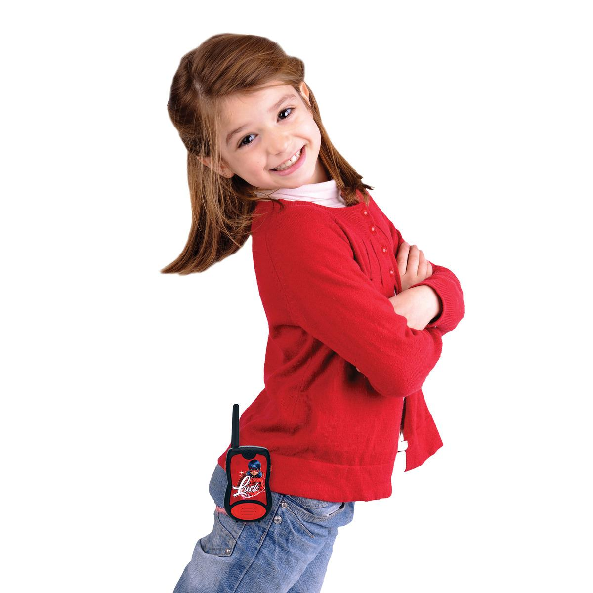 Una bambina con maglione rosso e jeans indossa un walkie-talkie alla cintura.