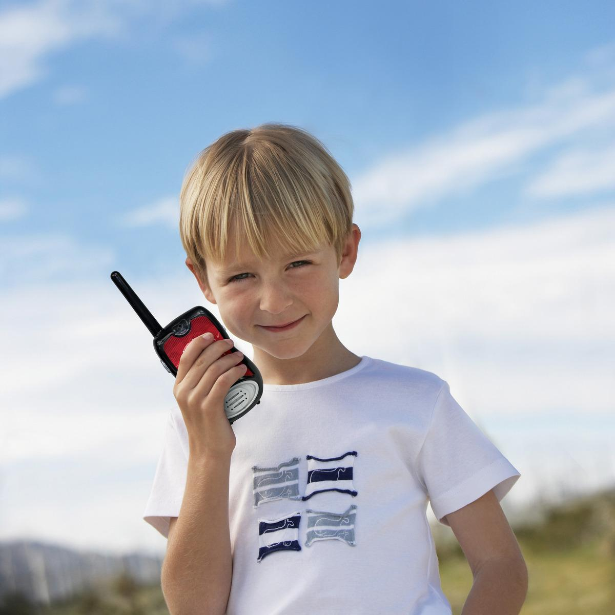 Un ragazzo biondo tiene un walkie-talkie rosso e nero contro il cielo azzurro.