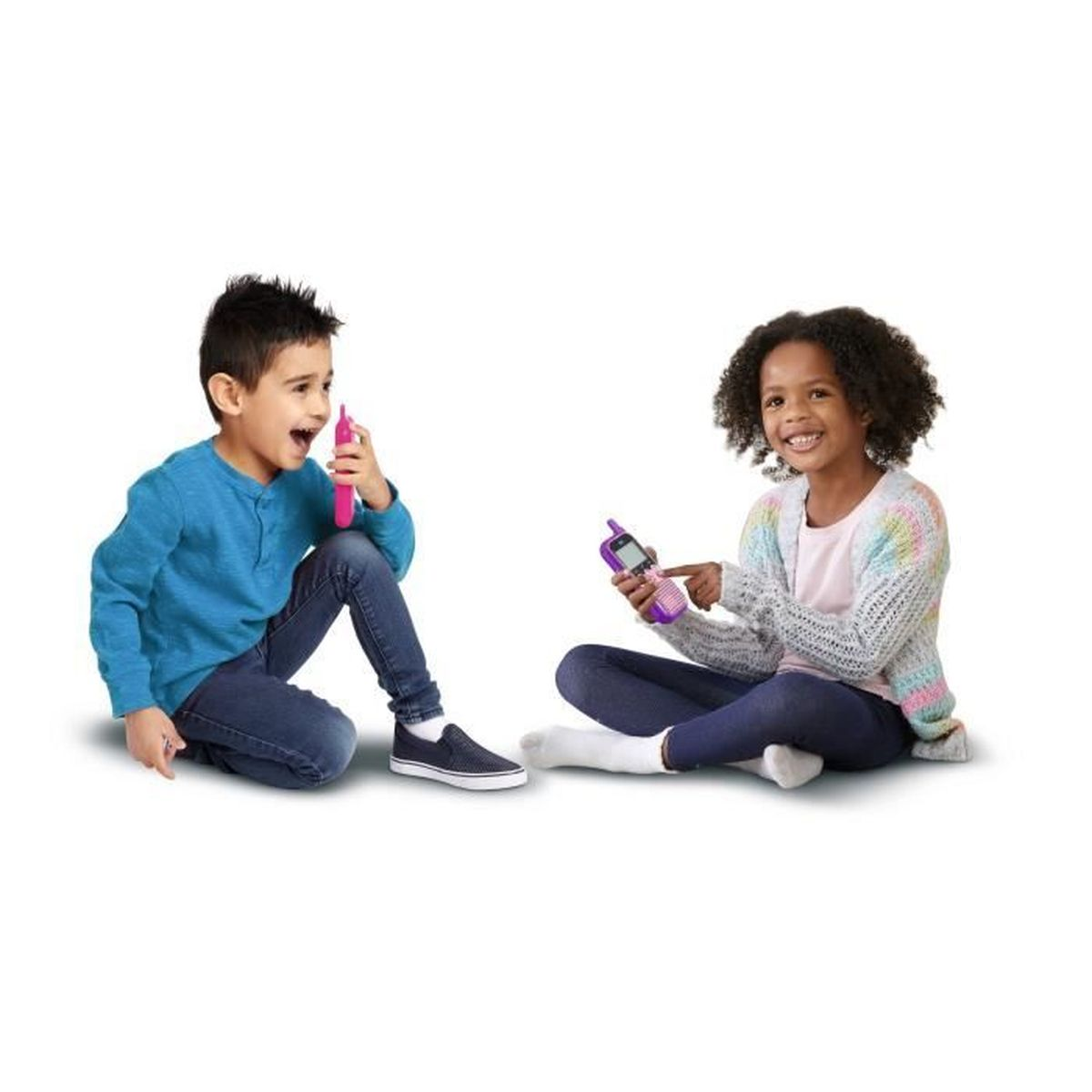 Due bambini seduti giocano con telefoni giocattolo. Ragazzo parla nel dispositivo rosa, ragazza indica dispositivo viola.