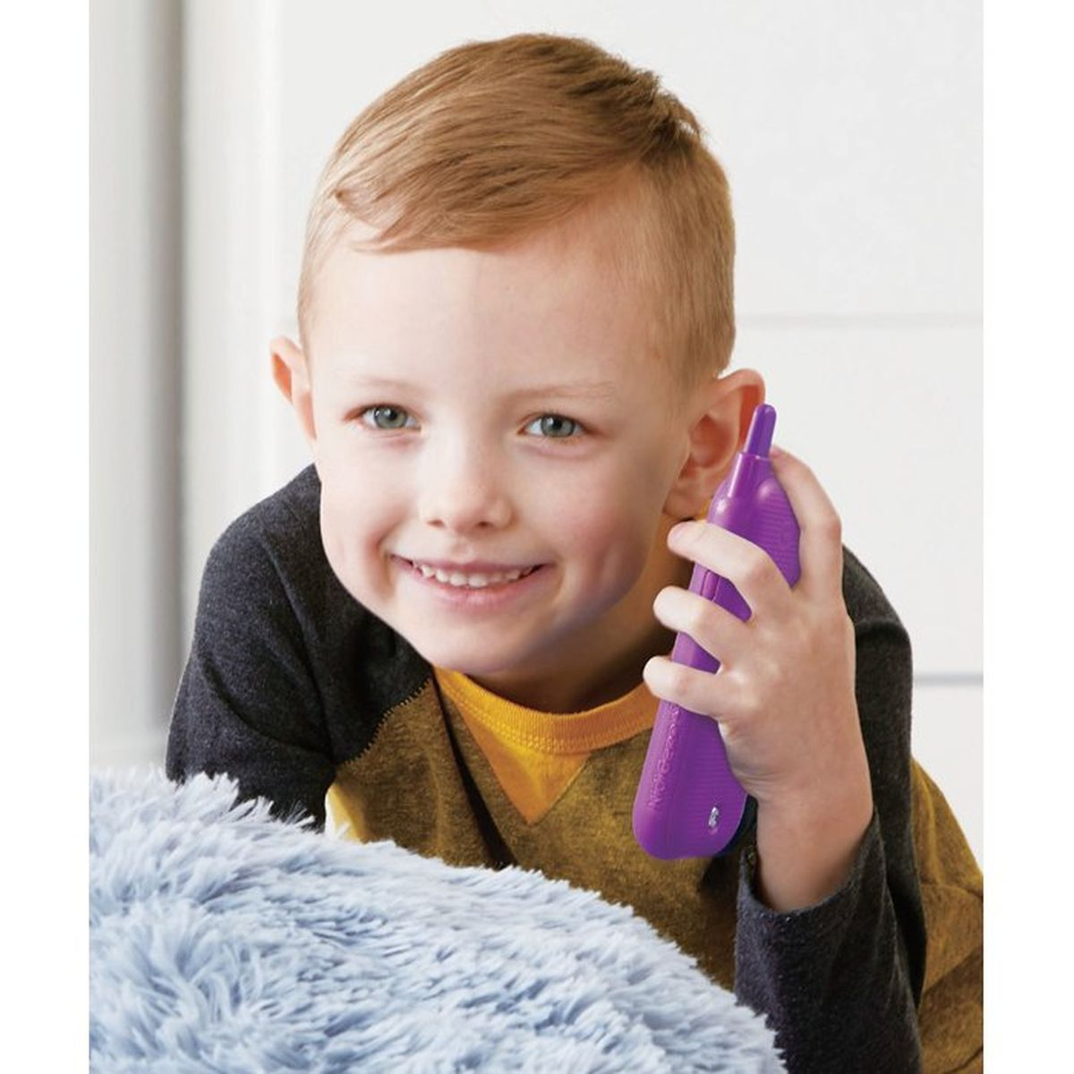 Un bambino sorride tenendo un telefono giocattolo viola all'orecchio.
