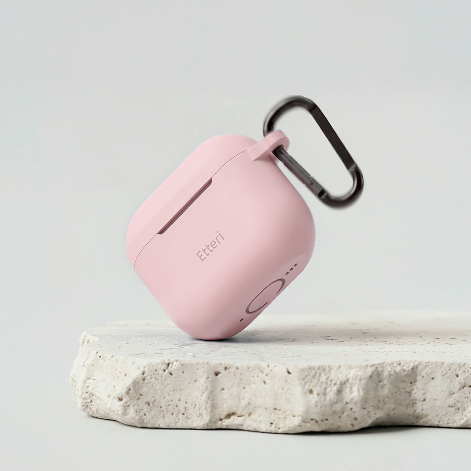 Una custodia di ricarica rosa per auricolari con moschettone, appoggiata su una pietra.