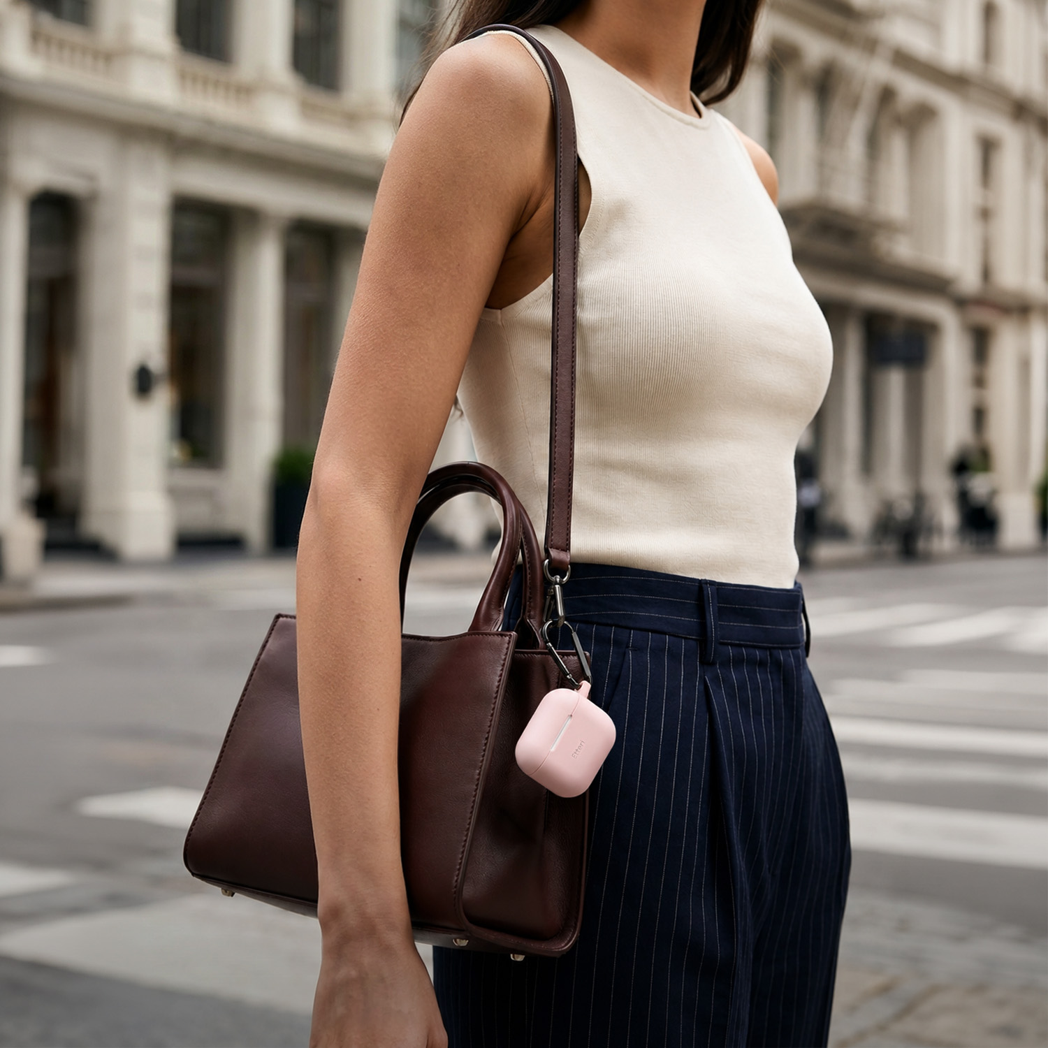 Donna con borsa marrone e custodia rosa, davanti a edifici in strada.