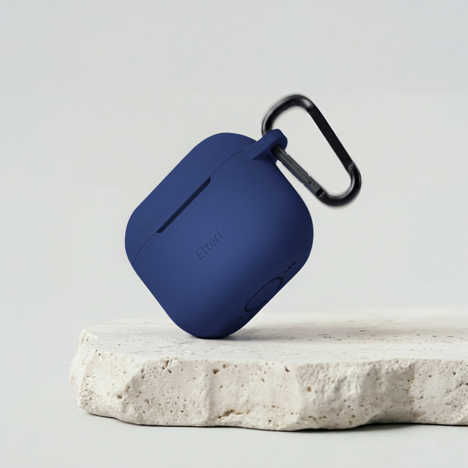 Custodia blu scuro per auricolari con moschettone nero su pietra.
