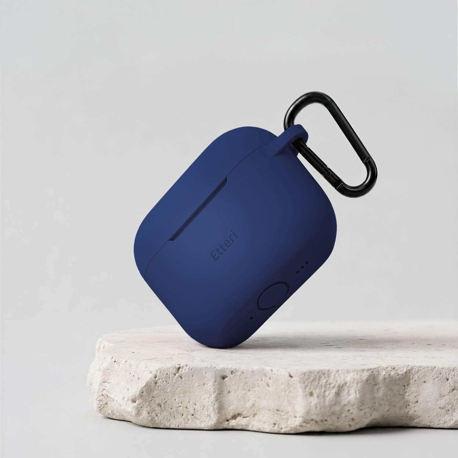 Una custodia blu navy per auricolari con moschettone nero poggia su una pietra grezza.