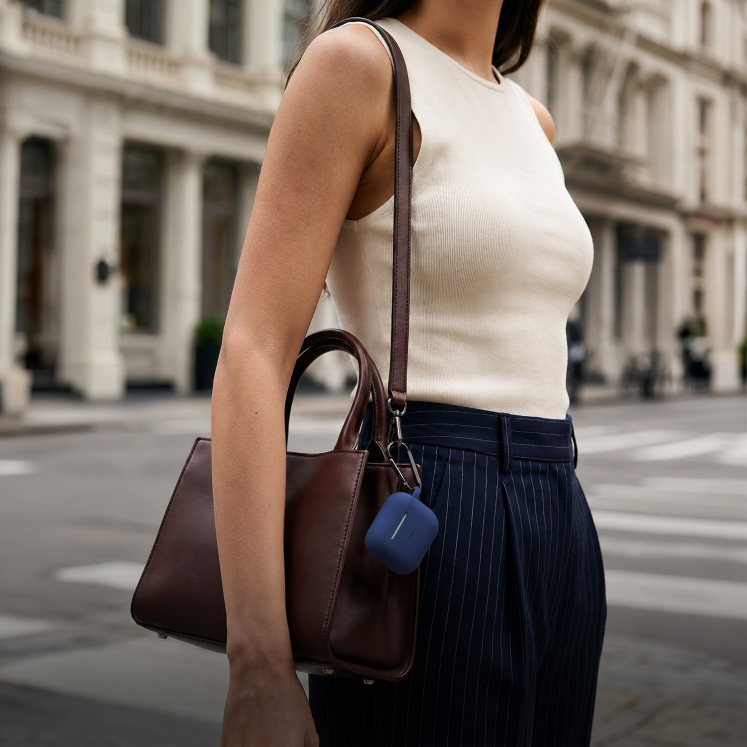 Donna con top bianco e pantaloni gessati porta una borsa marrone con custodia blu attaccata.